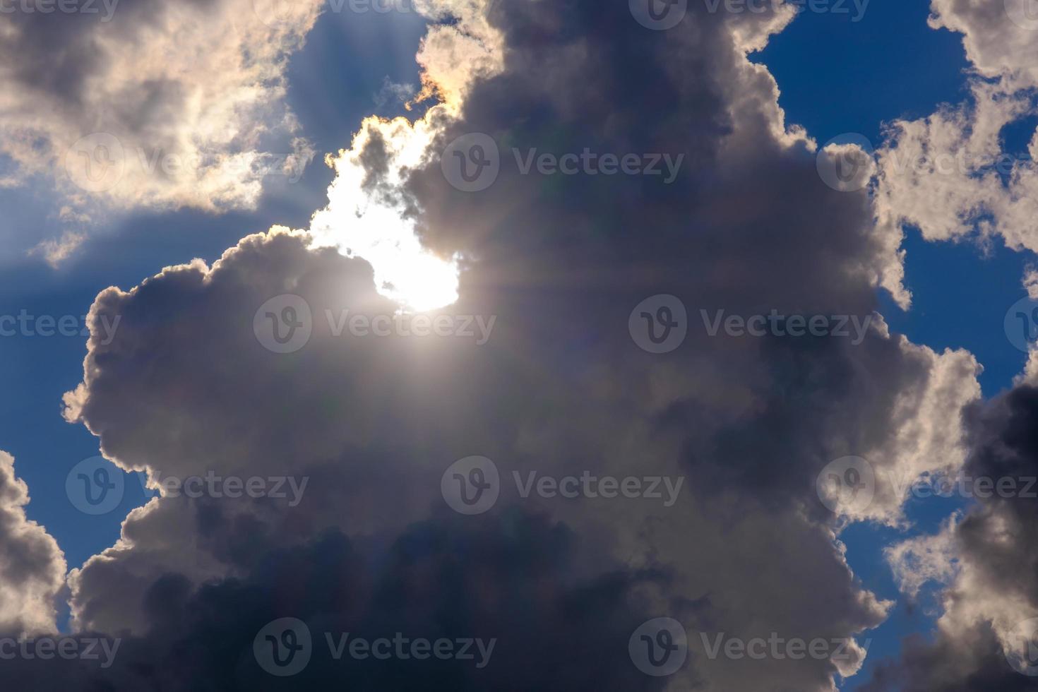 dramatic white and dark clouds in the blue sky with sun rays breaking through photo