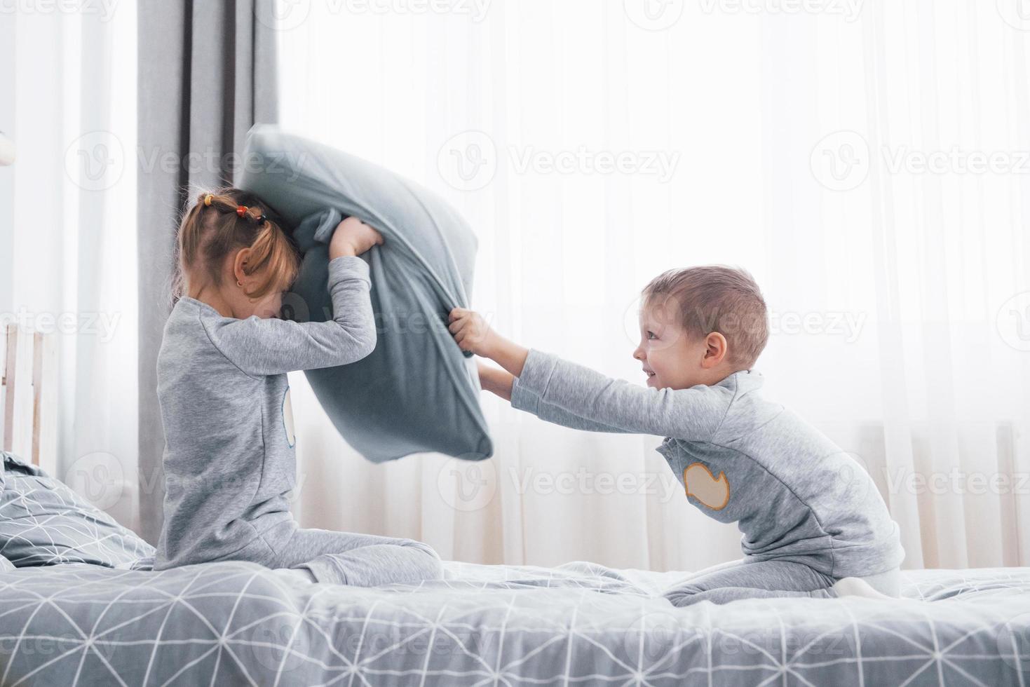 niño y niña organizaron una pelea de almohadas en la cama del dormitorio. los niños traviesos se golpean las almohadas. les gusta ese tipo de juego foto