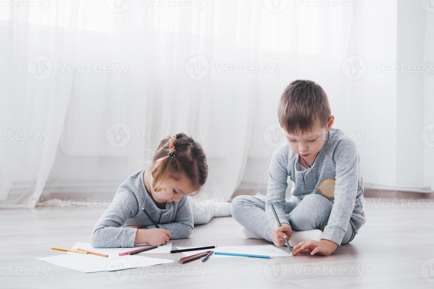 Children lie on the floor in pajamas and draw with pencils. Cute child painting by pencils photo