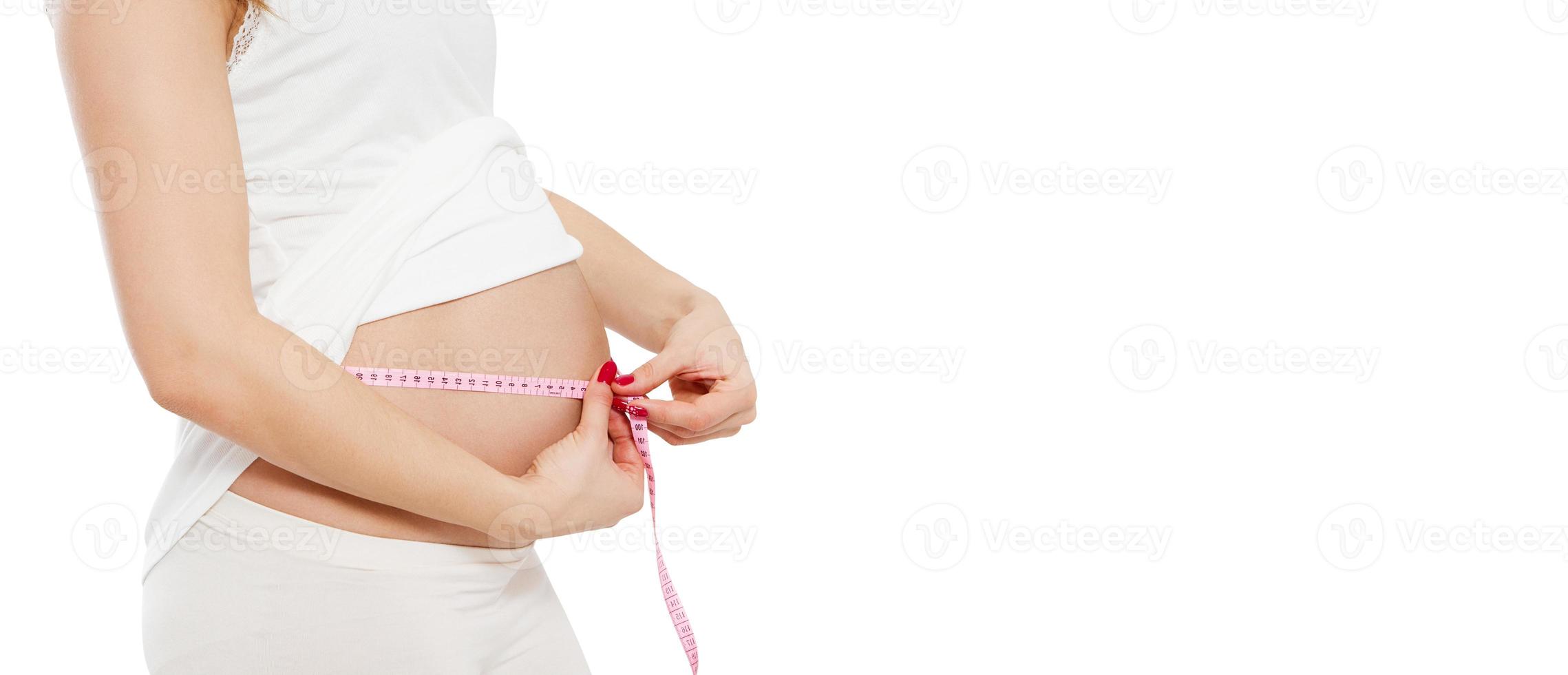 Pregnant woman measuring her belly isolated on white. Beautiful pregnant young woman in casual clothes is measuring her bare tummy cropped image photo