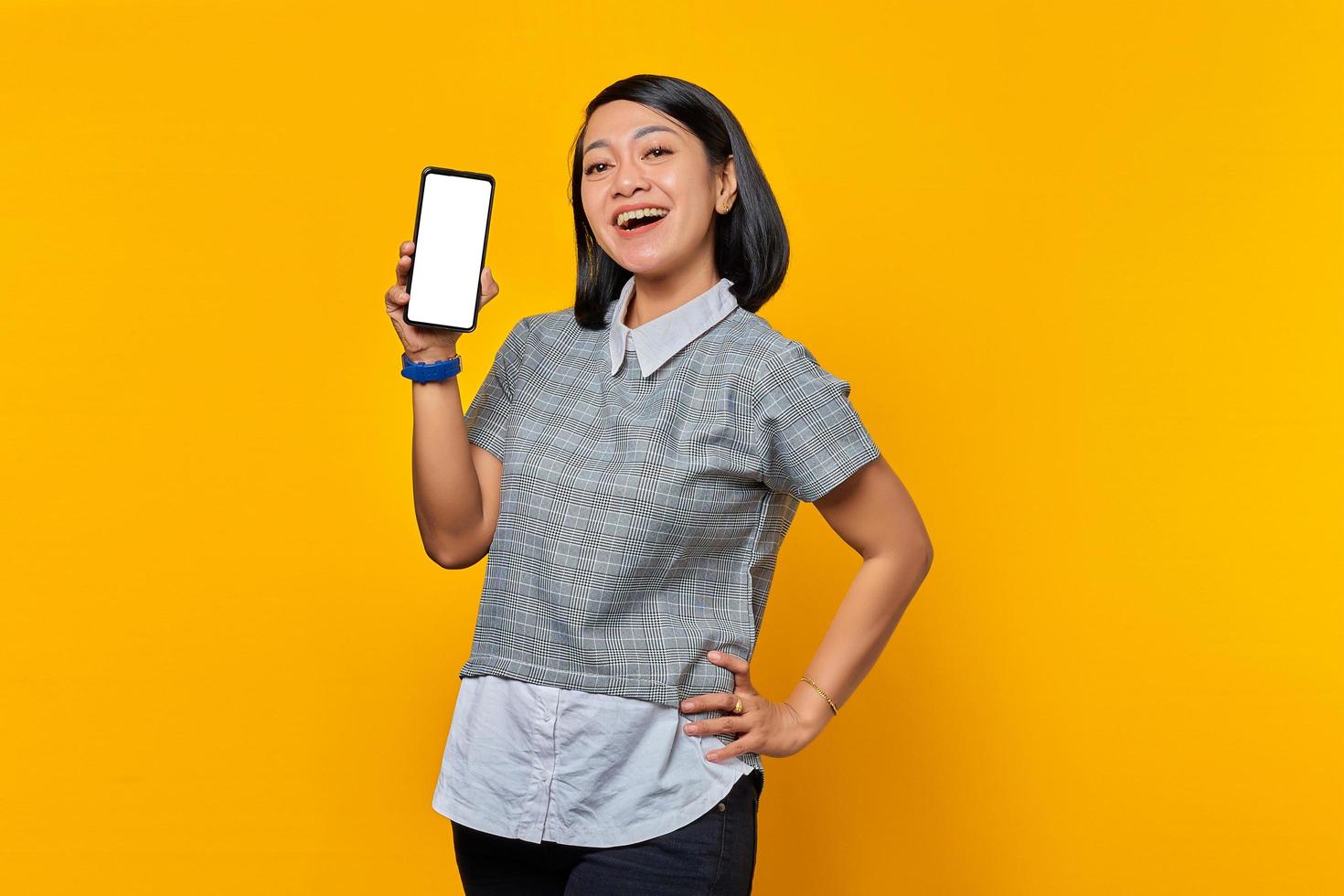 Cheerful Asian woman showing smartphone blank screen over yellow background photo