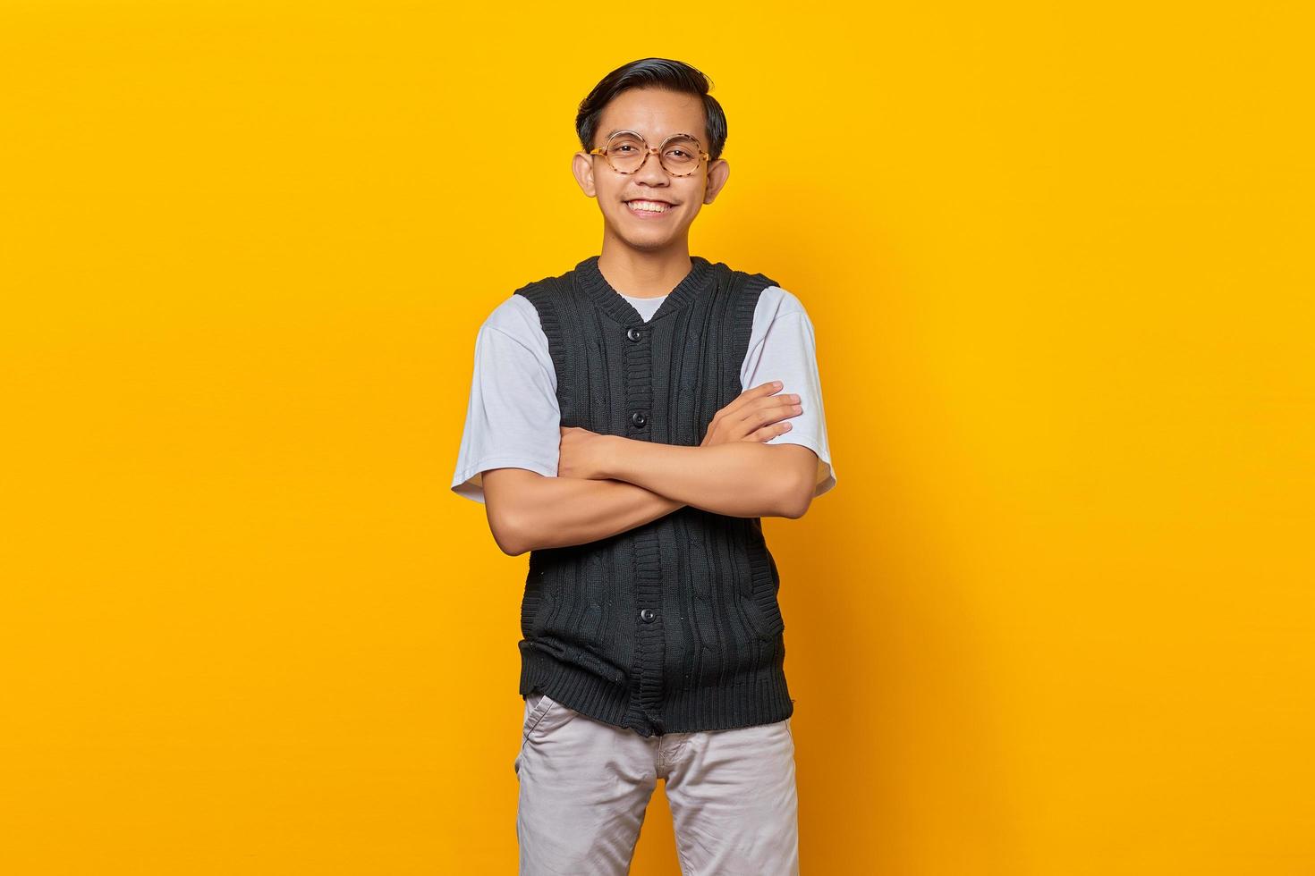 Portrait of smiling young Asian man looking at camera with crossed arms isolated on yellow background photo