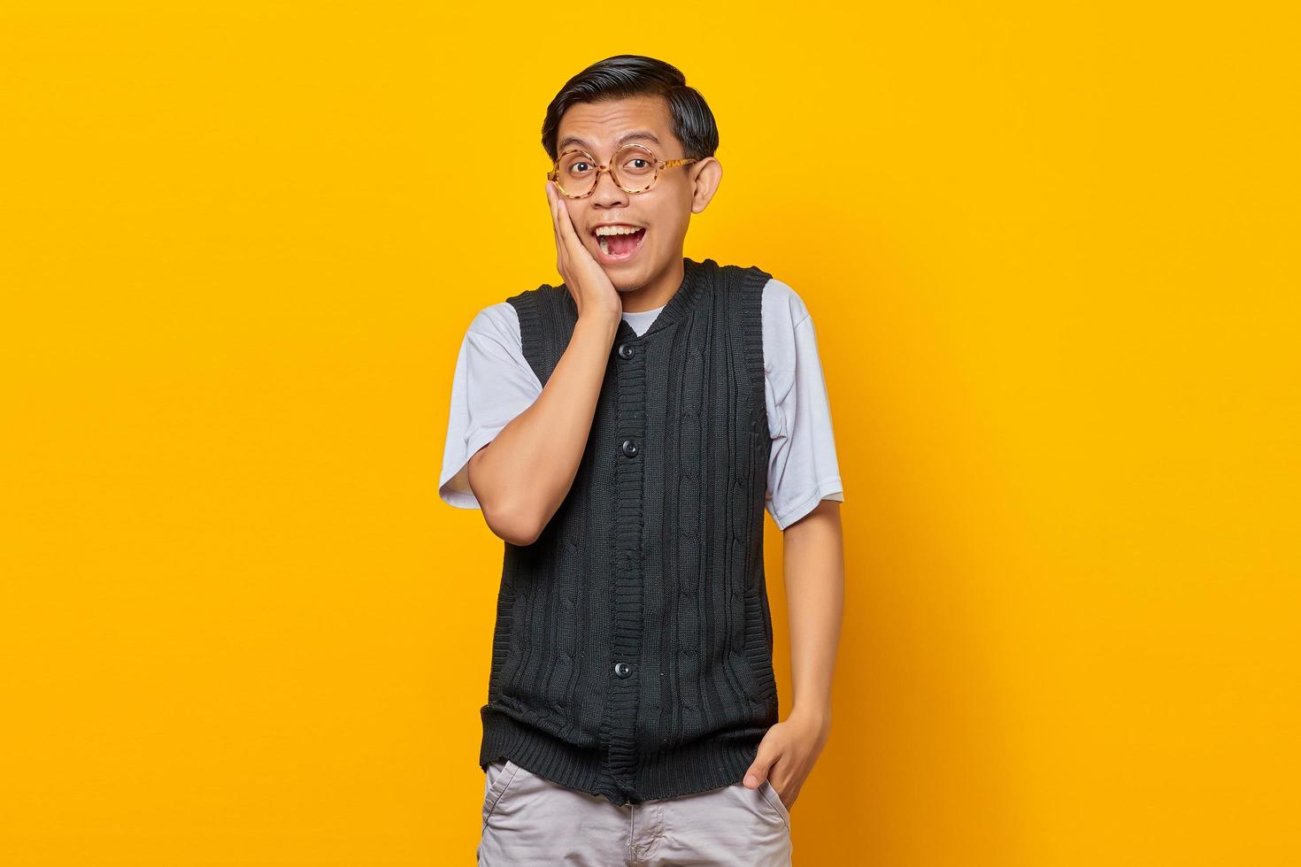 Portrait of surprised young Asian man looking at camera isolated on yellow background photo