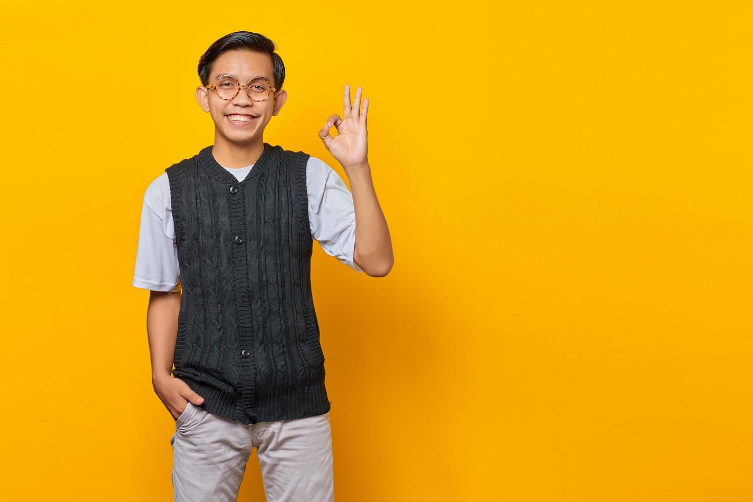 Portrait of handsome asian man showing ok gesture on yellow background photo