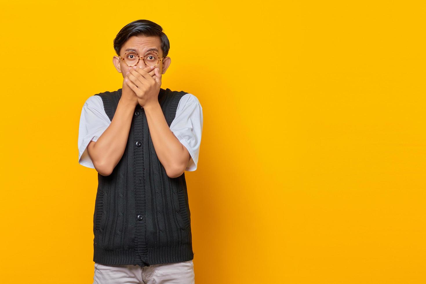 Retrato del joven asiático sorprendido cubriendo la boca con la mano por error sobre fondo amarillo foto