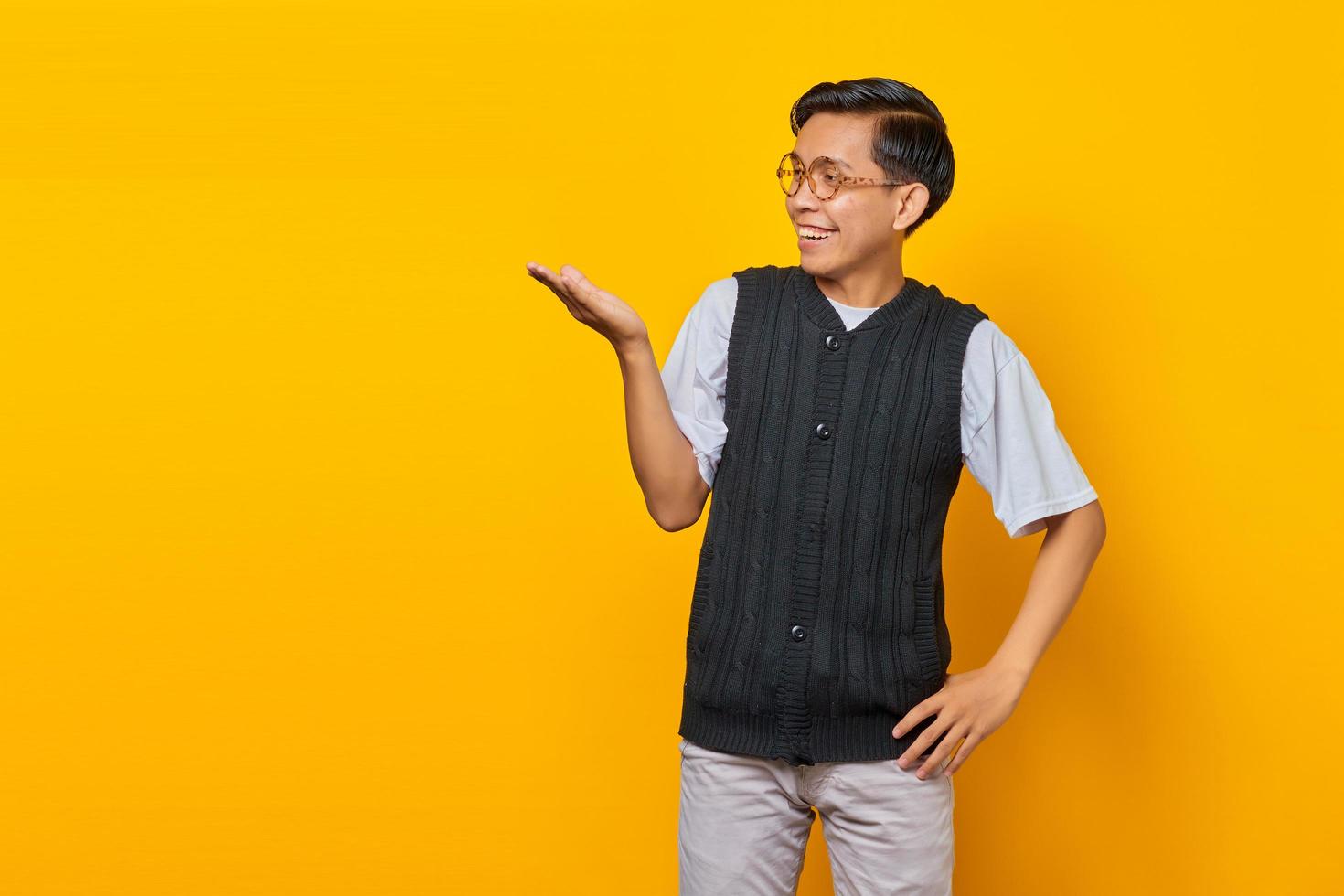 Portrait of smiling handsome young man showing copy space in palm on yellow background photo