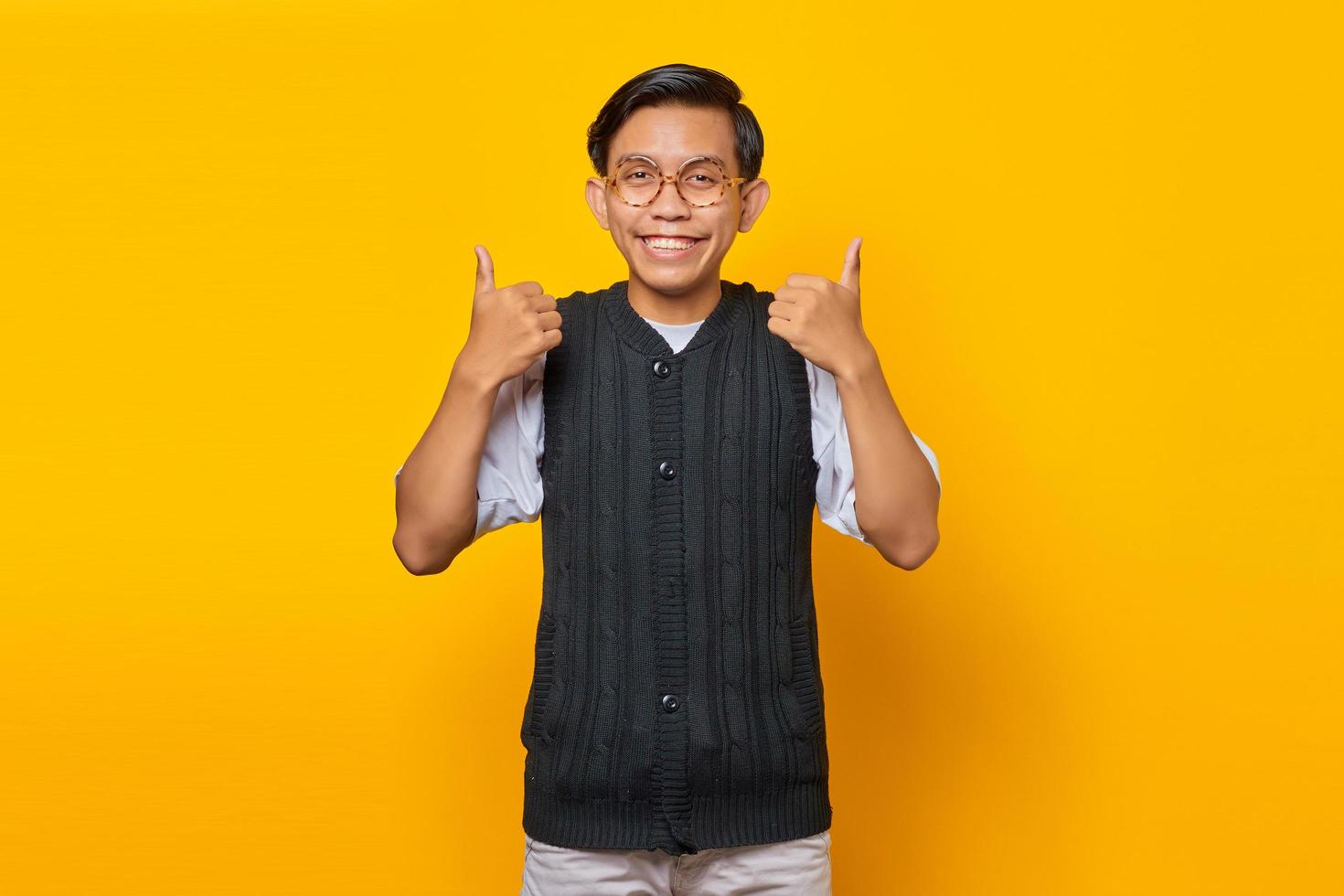 Portrait of cheerful young Asian man showing thumbs up or approval sign isolated on yellow background photo