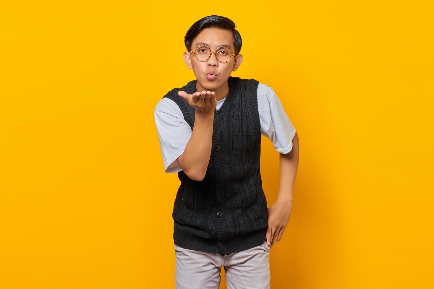 Portrait of charming young Asian man holding palms sending air kiss to girlfriend photo