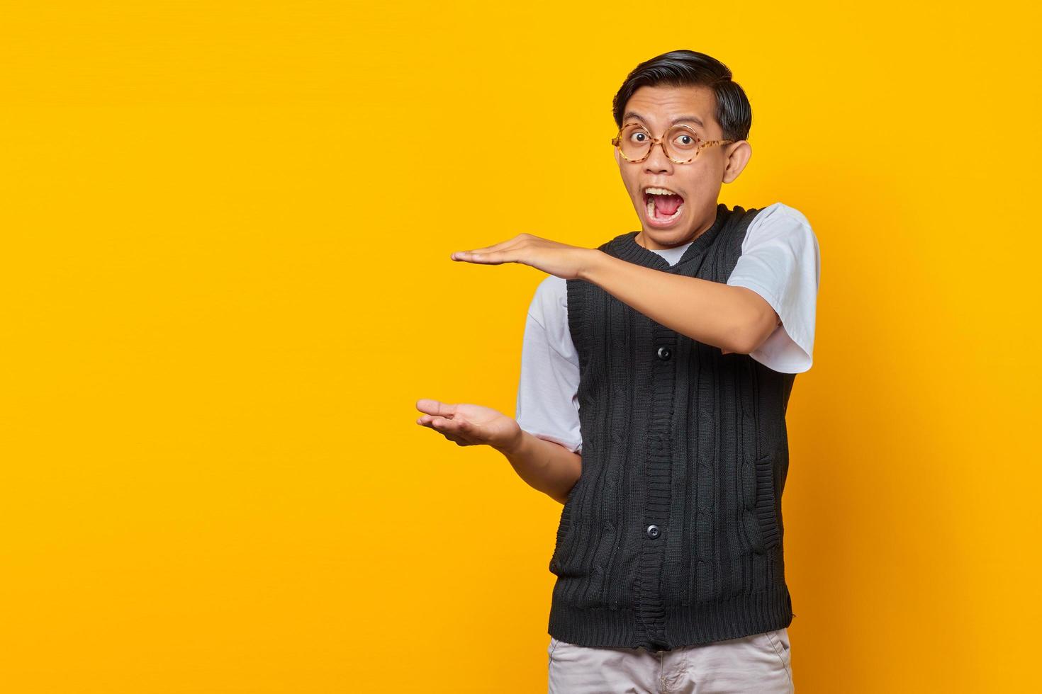 Shocked asian man showing product over yellow background photo