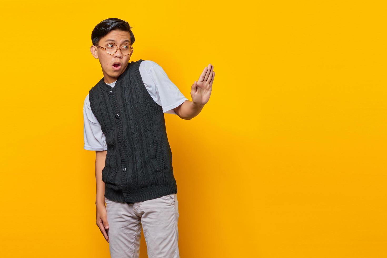 Young Asian man doing stop gesture with hands palms isolated over yellow background photo