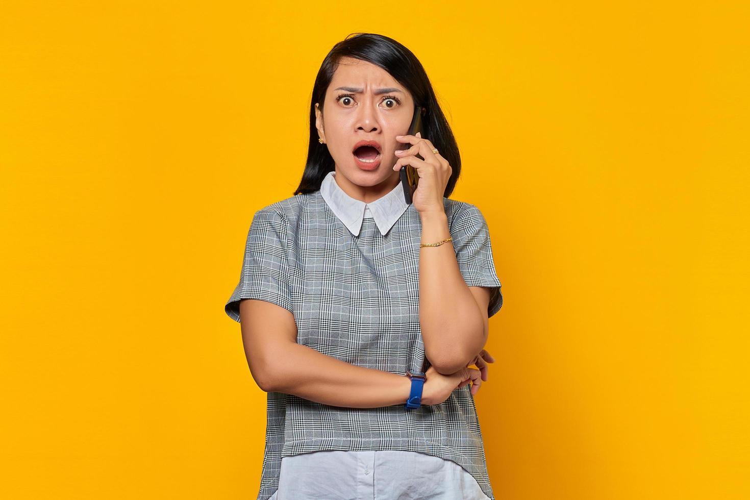 Retrato de una joven asiática sorprendida mientras recibe una llamada entrante en el teléfono inteligente sobre fondo amarillo foto