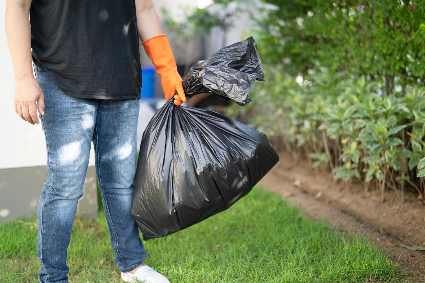 Woman holding black plastic trash bin bags of garbage on the pavement, clean environment concept. photo