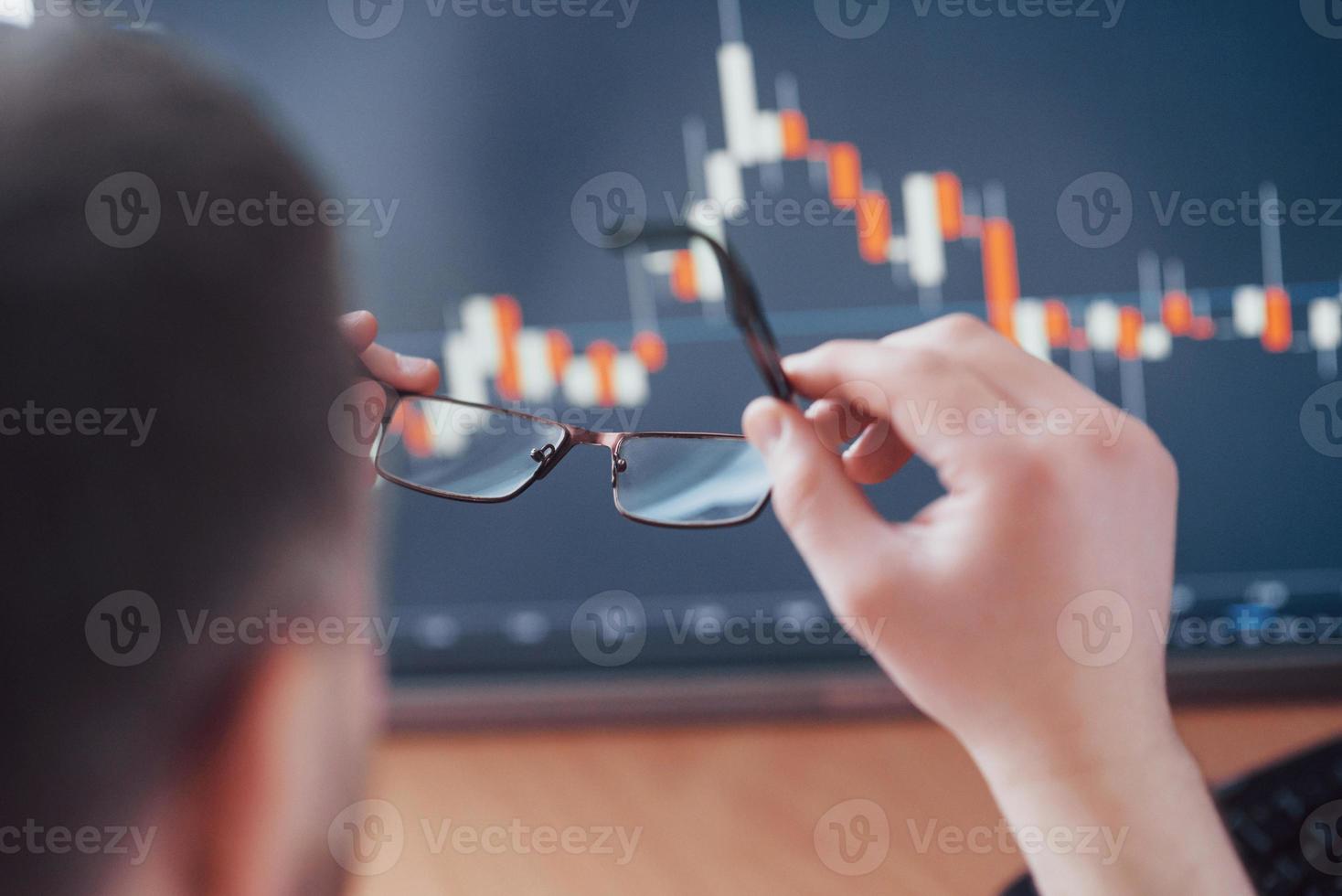 Analyzing data. Close up of a young businessman who holds glasses and looks at the gff while working in a creative office photo