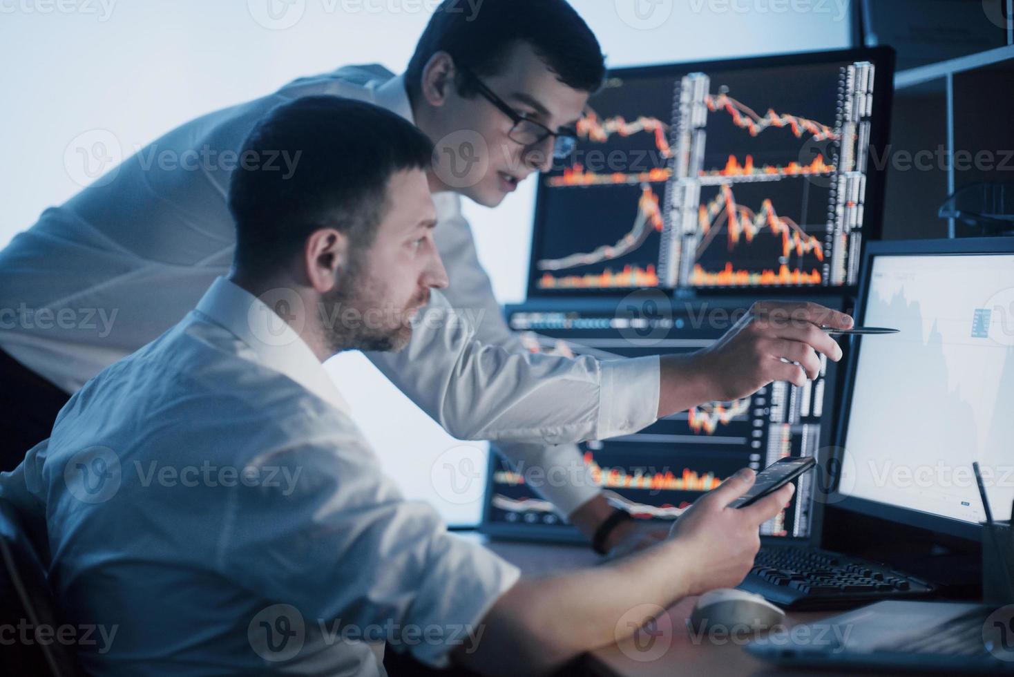 Team of stockbrokers are having a conversation in a dark office with display screens. Analyzing data, graphs and reports for investment purposes. Creative teamwork traders photo