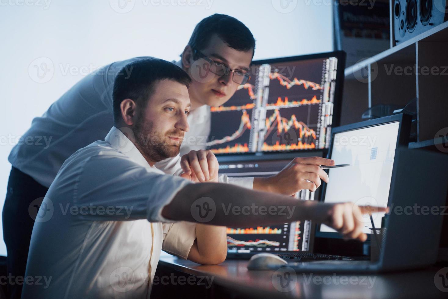 Team of stockbrokers are having a conversation in a dark office with display screens. Analyzing data, graphs and reports for investment purposes. Creative teamwork traders photo
