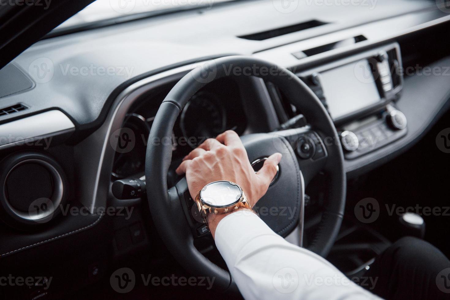 A young man sits in a newly bought car holding his hands on a rudder photo