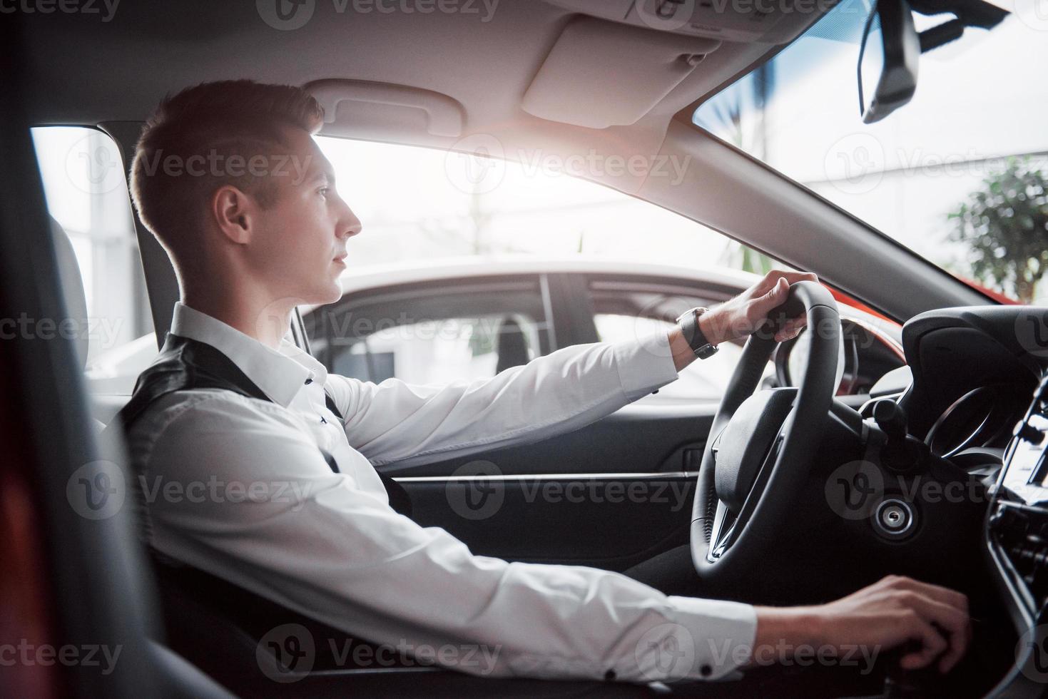 un joven sentado al volante en un automóvil recién comprado, una compra exitosa. foto
