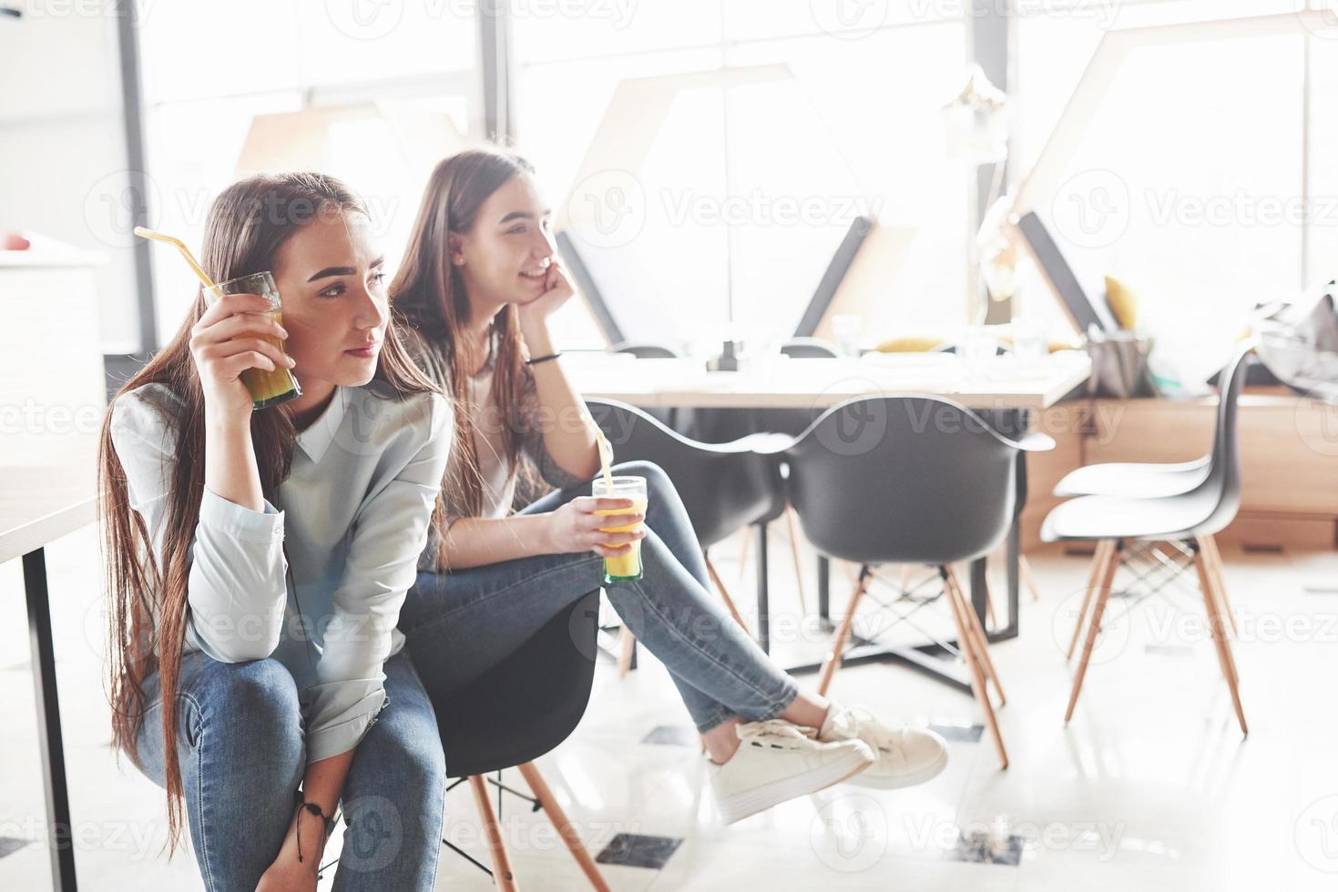 Two beautiful twin girls spend time drinking juice. Sisters relaxing in a cafe and having fun together photo