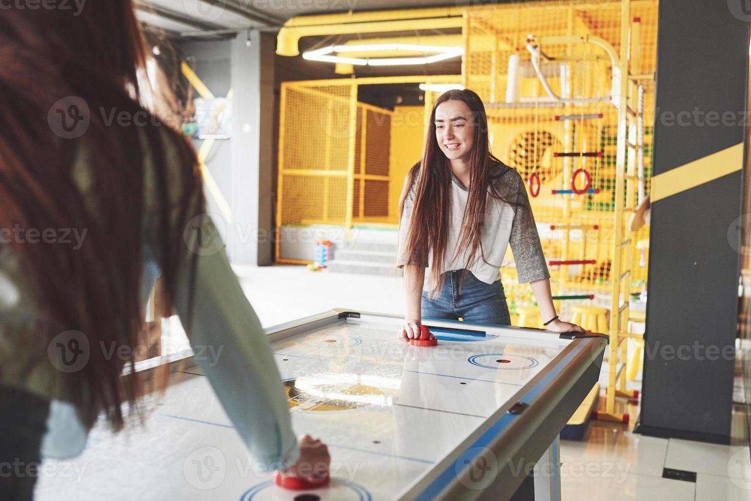 Two beautiful twin girls play air hockey in the game roomand have fun photo