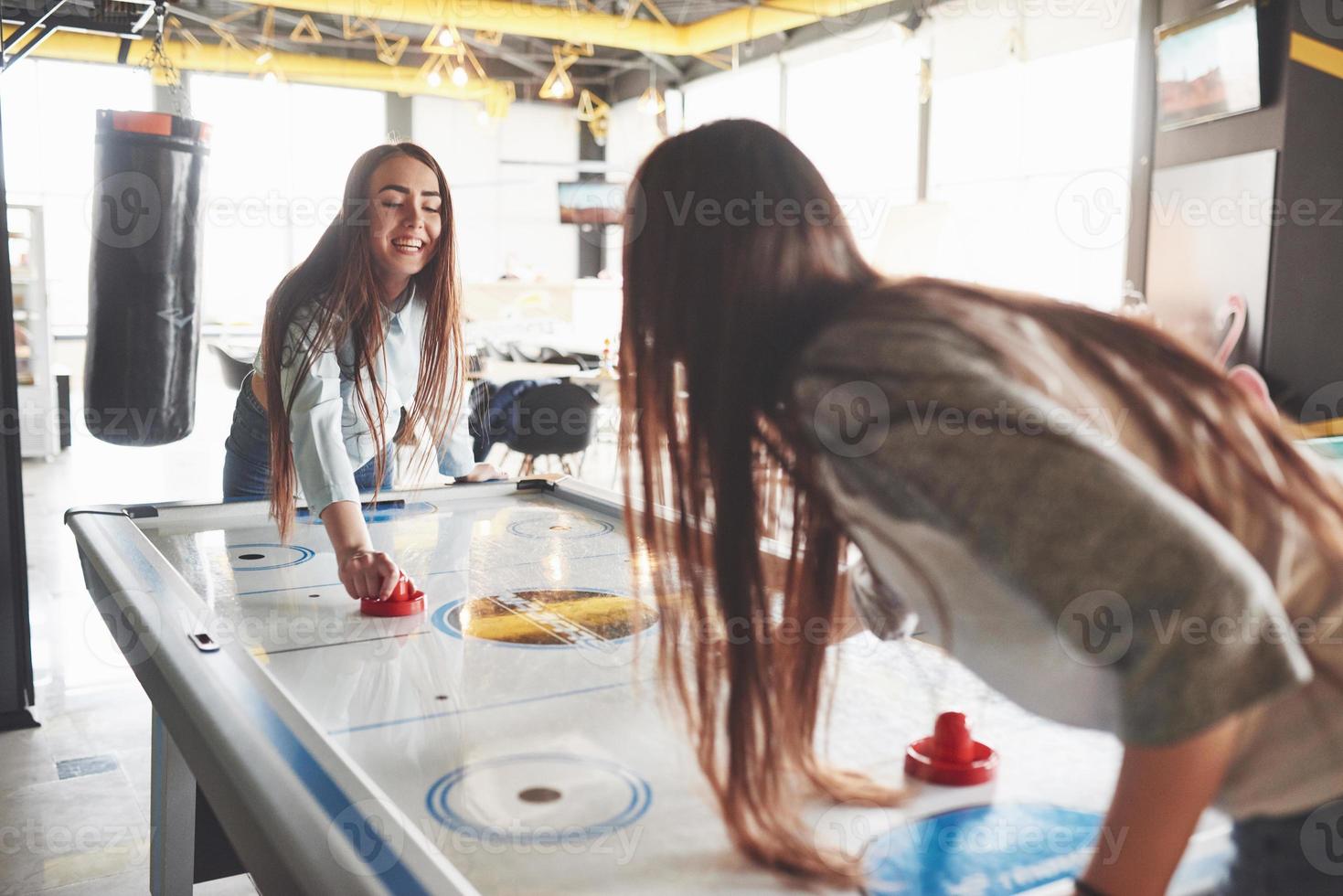 Two beautiful twin girls play air hockey in the game roomand have fun photo