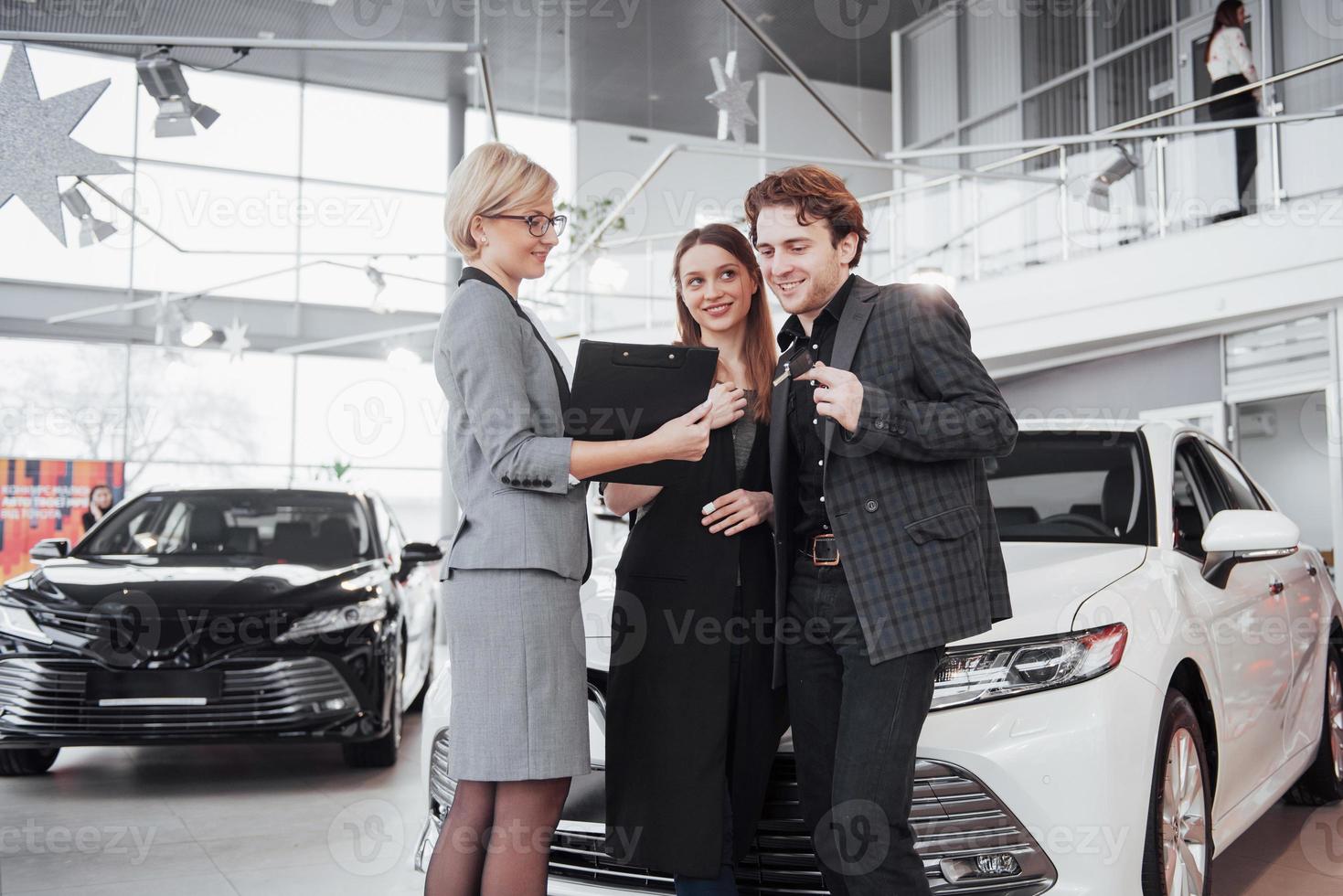 Proud owners. Beautiful young happy couple hugging standing near their newly bought car smiling joyfully showing car keys to the camera copyspace family love relationship lifestyle buying consumerism photo