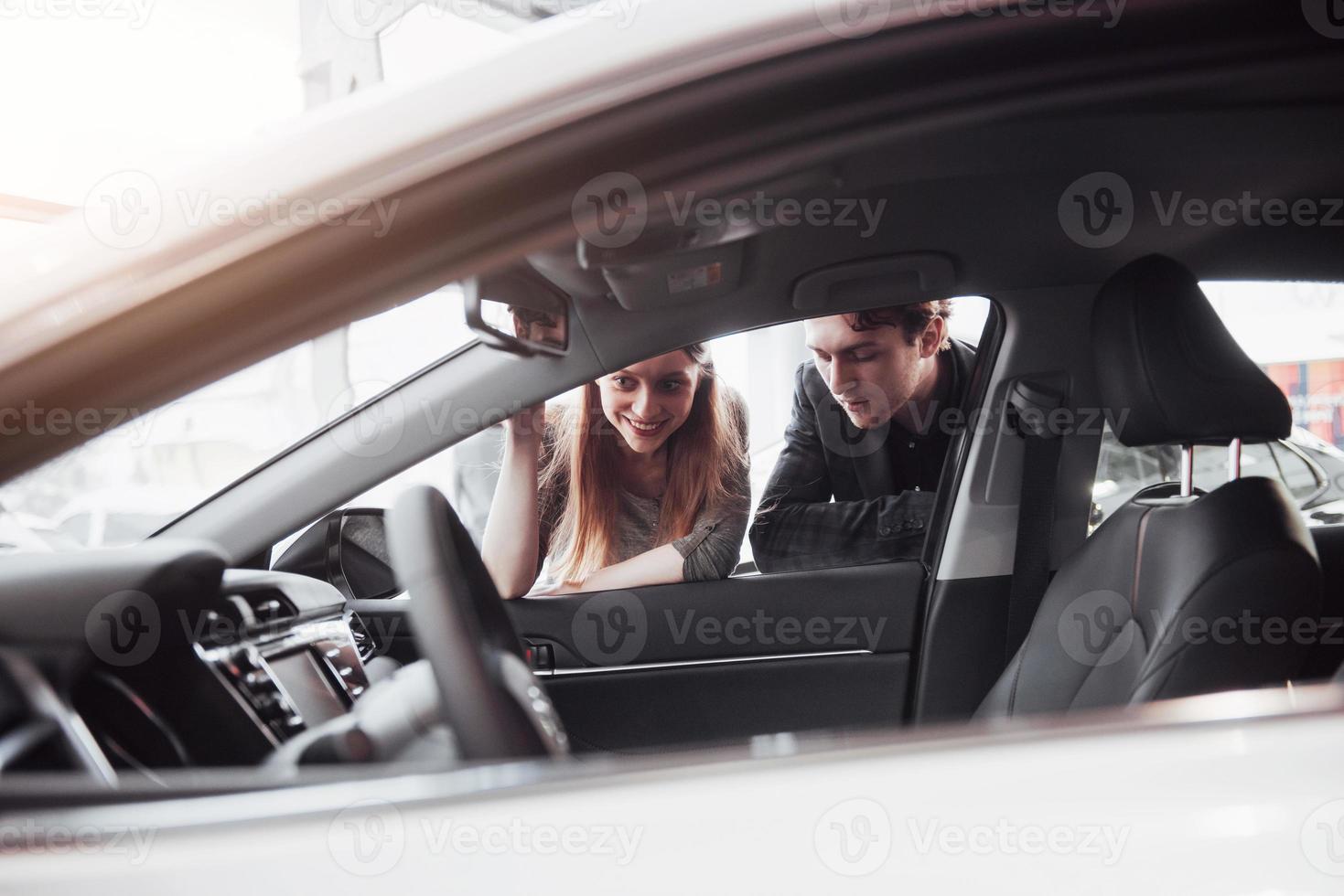 me gusta este coche. Hermosa joven pareja de pie en el concesionario eligiendo el coche para comprar foto