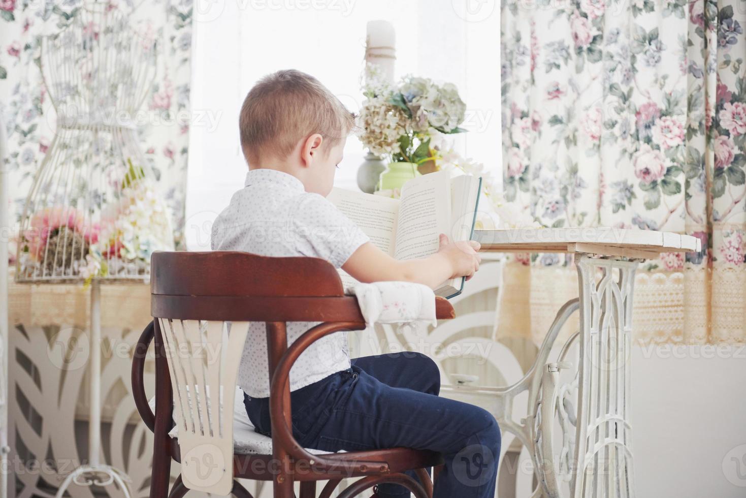 education, childhood, people, homework and school concept - bored student boy reading book or textbook at home photo