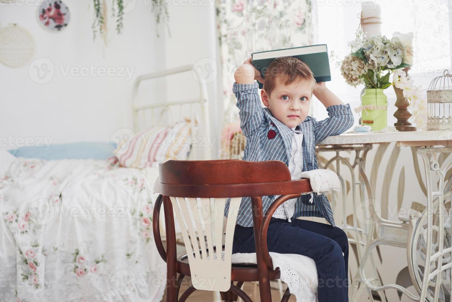 Photo of diligent schoolboy with book on his head doing homework