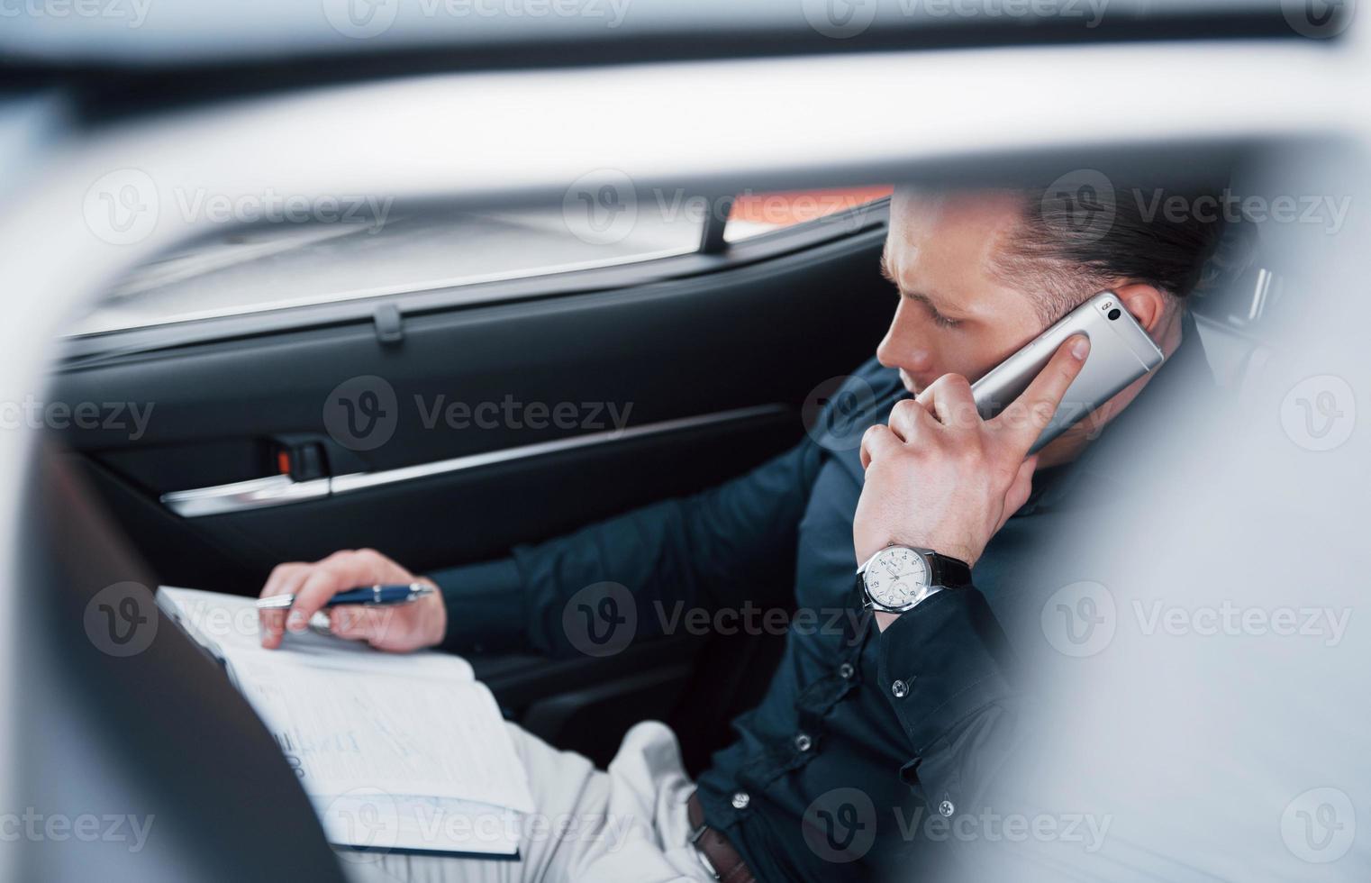 un joven empresario arregla sus asuntos con un bloc de notas mientras está sentado en la parte trasera del automóvil foto