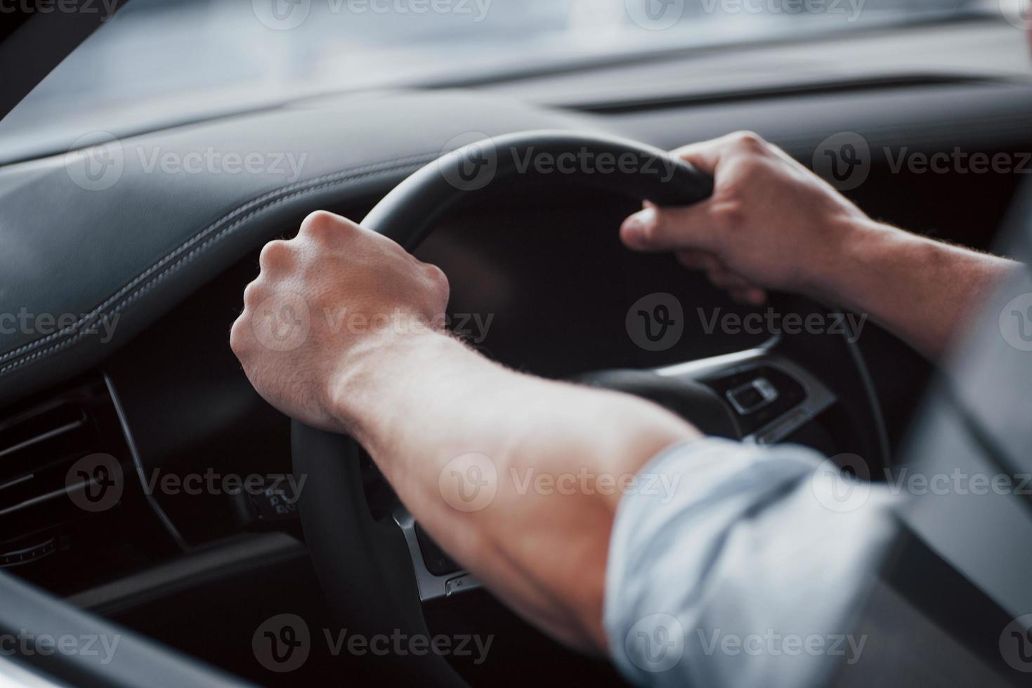 A young man sits in a newly bought car holding his hands on a rudder. photo