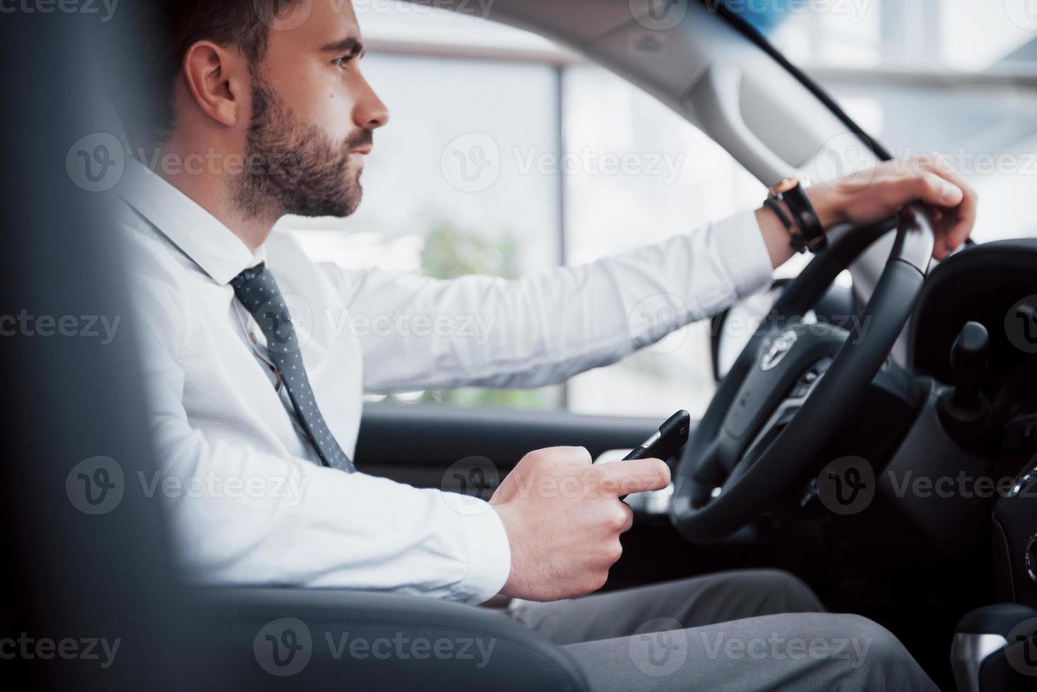 Hombre de negocios joven satisfecho mirando el teléfono móvil mientras conduce un coche foto