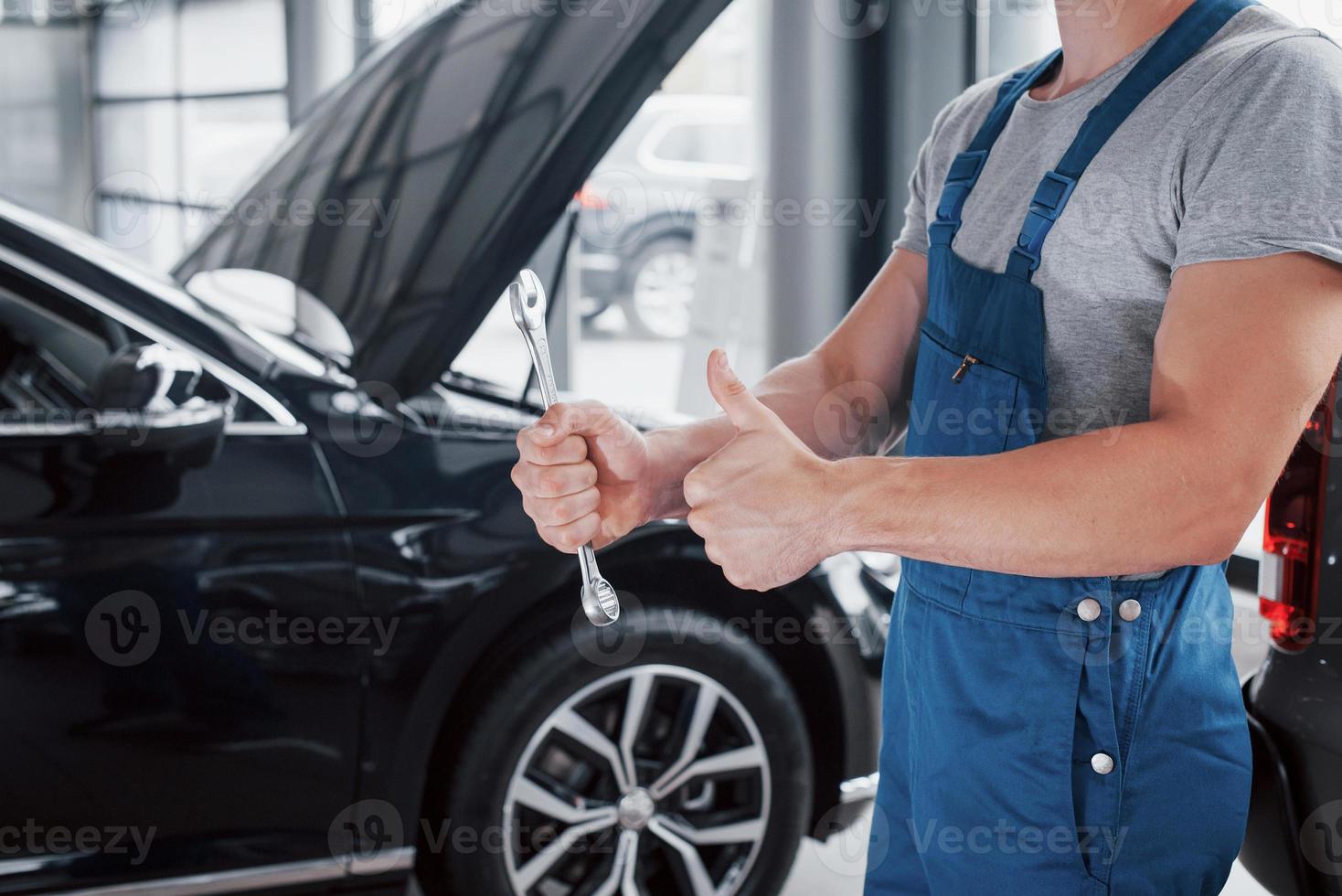 la mano de un mecánico de automóviles con una llave en una zona combinada cerca del automóvil en el taller. foto