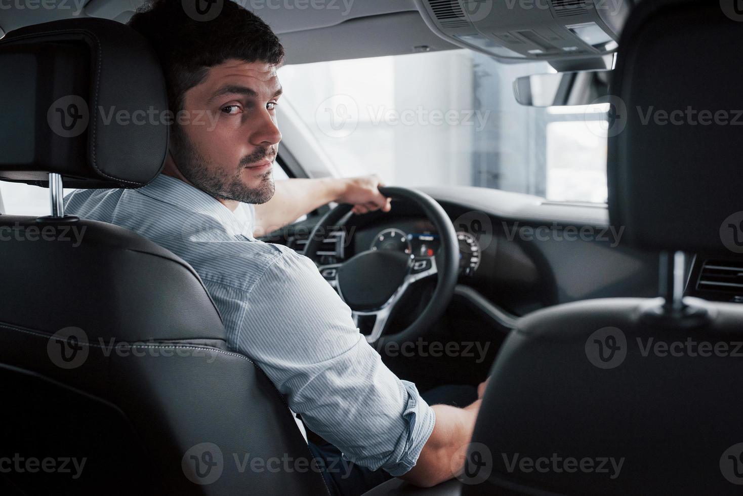 A young man sits in a newly bought car holding his hands on a rudder. photo