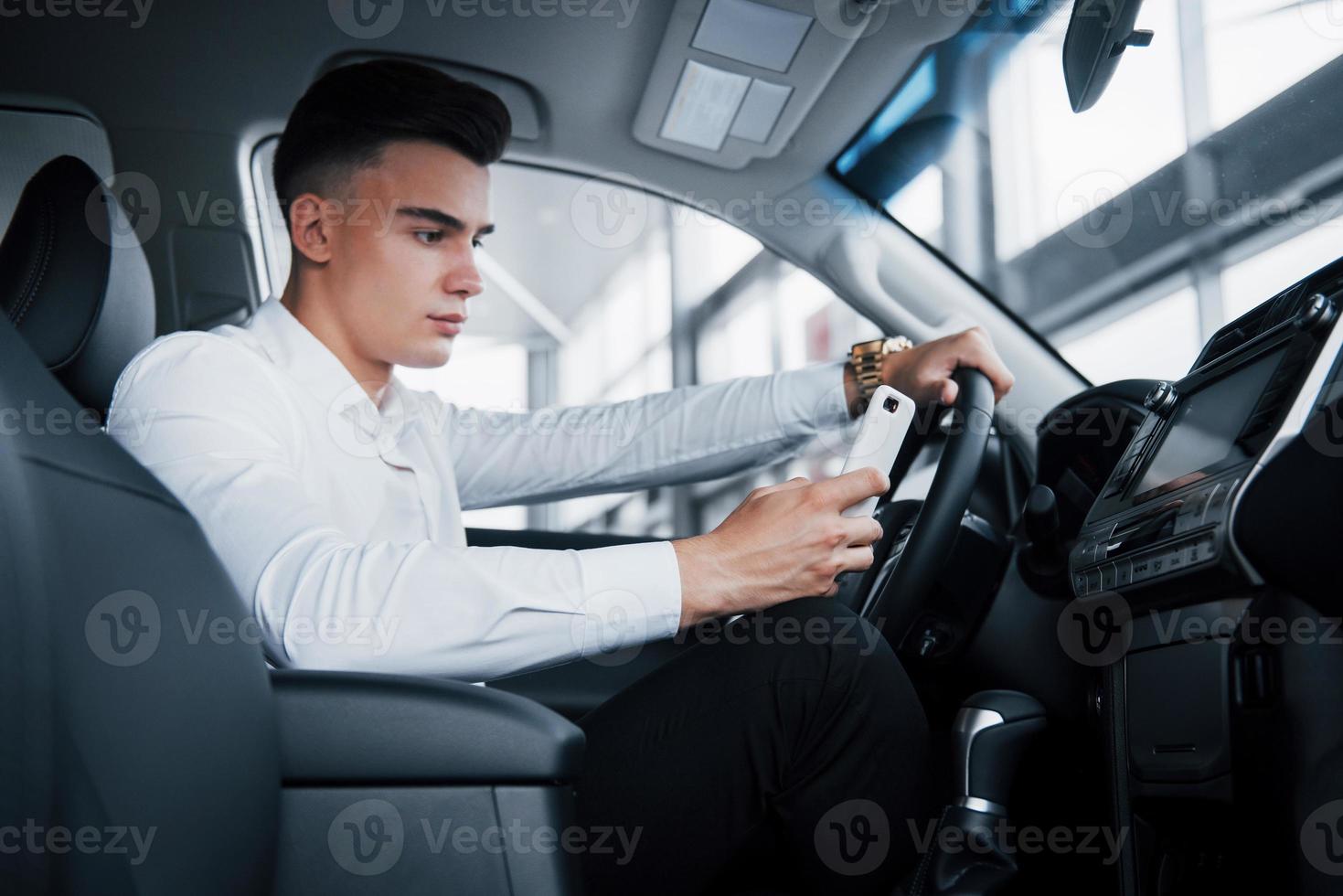 The handsome man is a buyer sitting in a car with a phone in a new car at a dealer center. photo