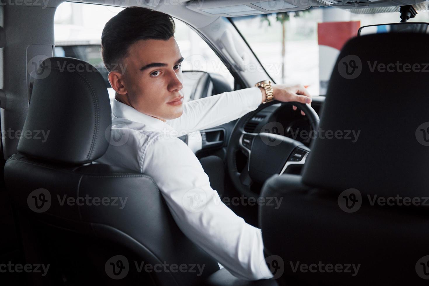 un joven sentado al volante en un automóvil recién comprado, una compra exitosa. foto