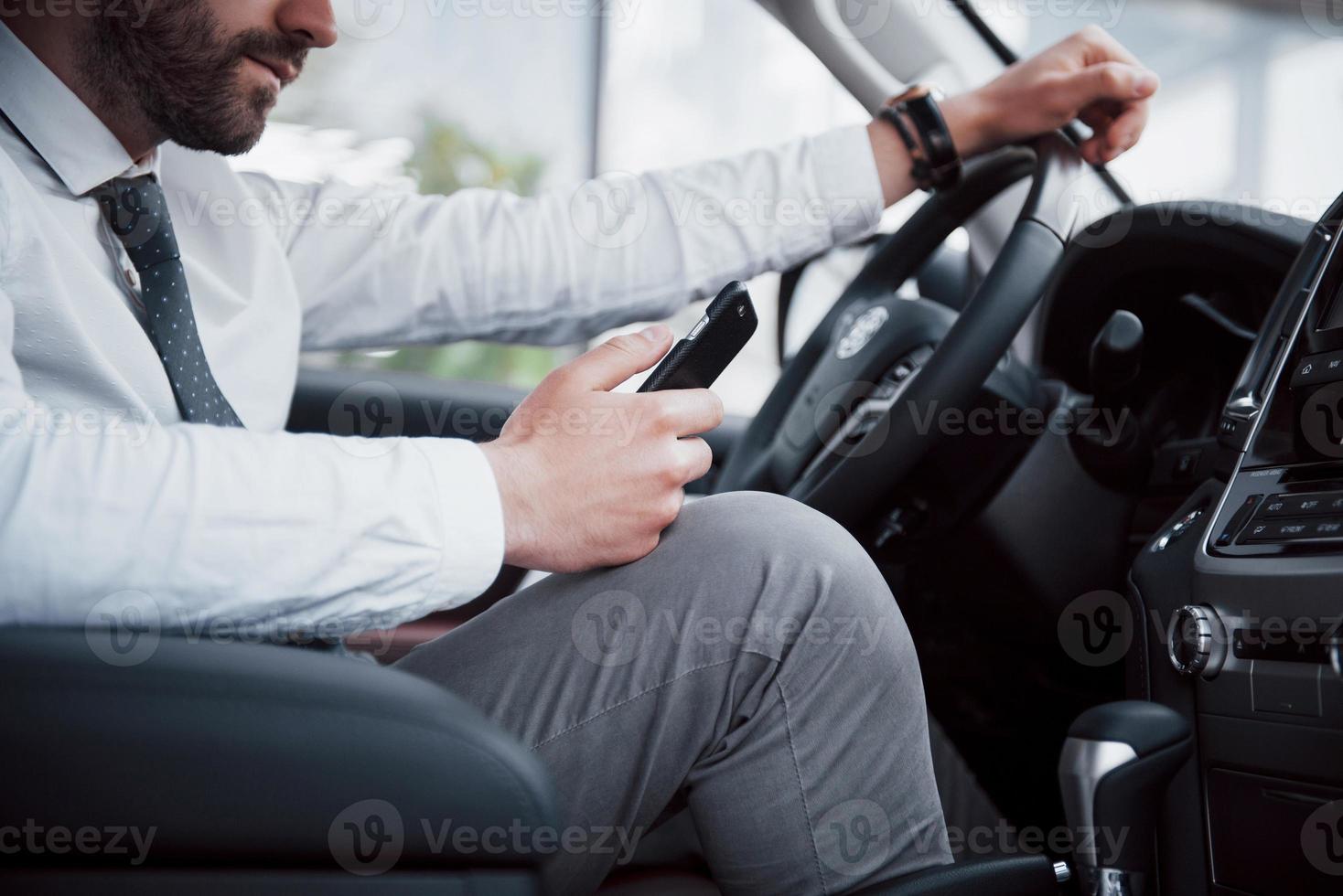 Hombre de negocios joven satisfecho mirando el teléfono móvil mientras conduce un coche foto