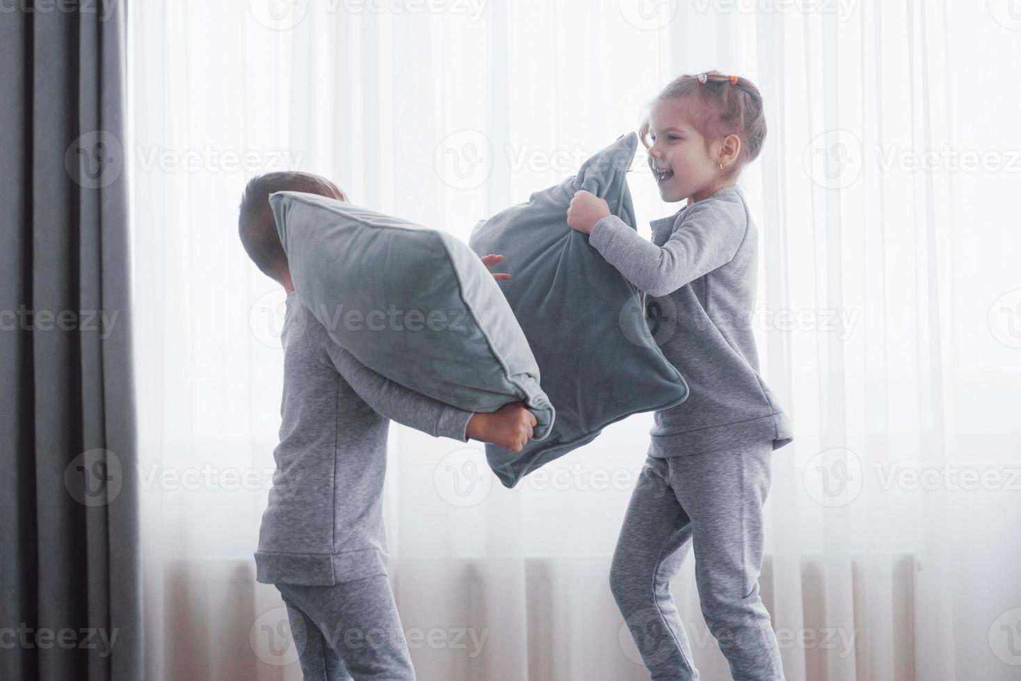 niño y niña organizaron una pelea de almohadas en la cama del dormitorio. los niños traviesos se golpean las almohadas. les gusta ese tipo de juego foto