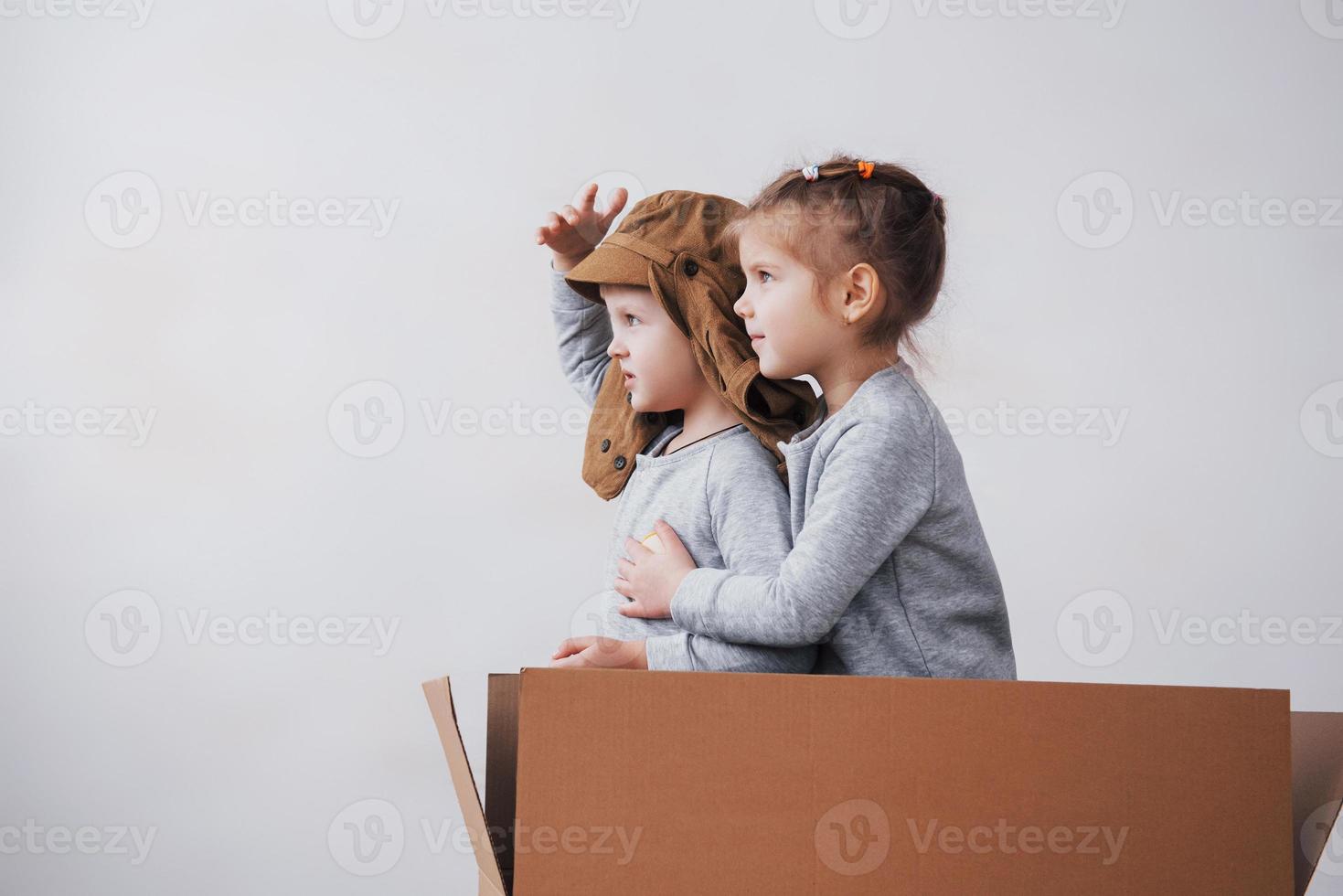 Playful childhood. Little boy having fun with cardboard box. Boy pretending to be pilot. Little boy and girl having fun at home photo