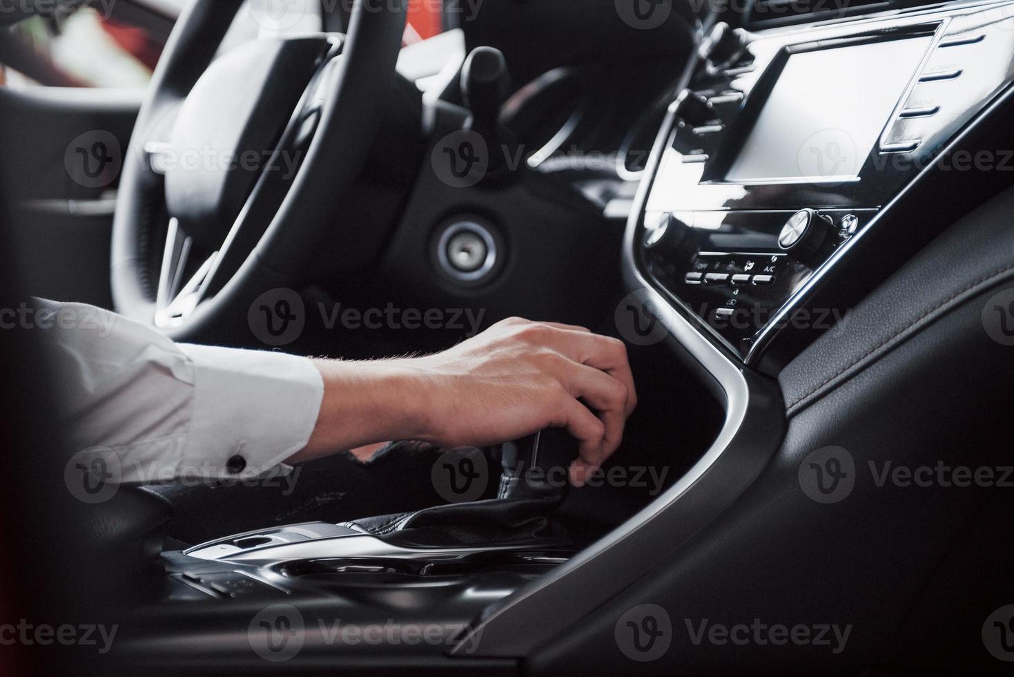 Cerca de un joven conduciendo un coche de carretera sosteniendo su mano sobre una caja de cambios. un empresario viaja en su coche. vista lateral, fondo. foto