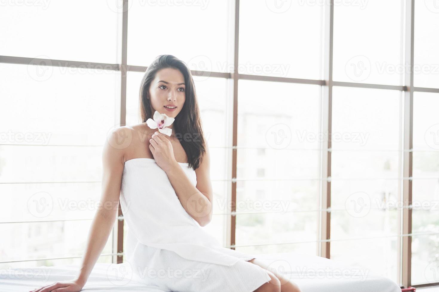 hermosa chica en una toalla con una orquídea, masaje de relajación esperando. foto