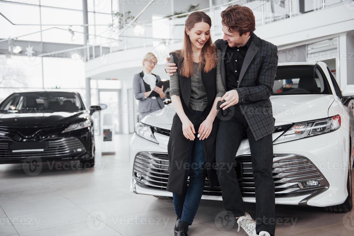 es el único coche que quiero. Hermosa joven pareja de pie en el concesionario eligiendo el coche para comprar foto