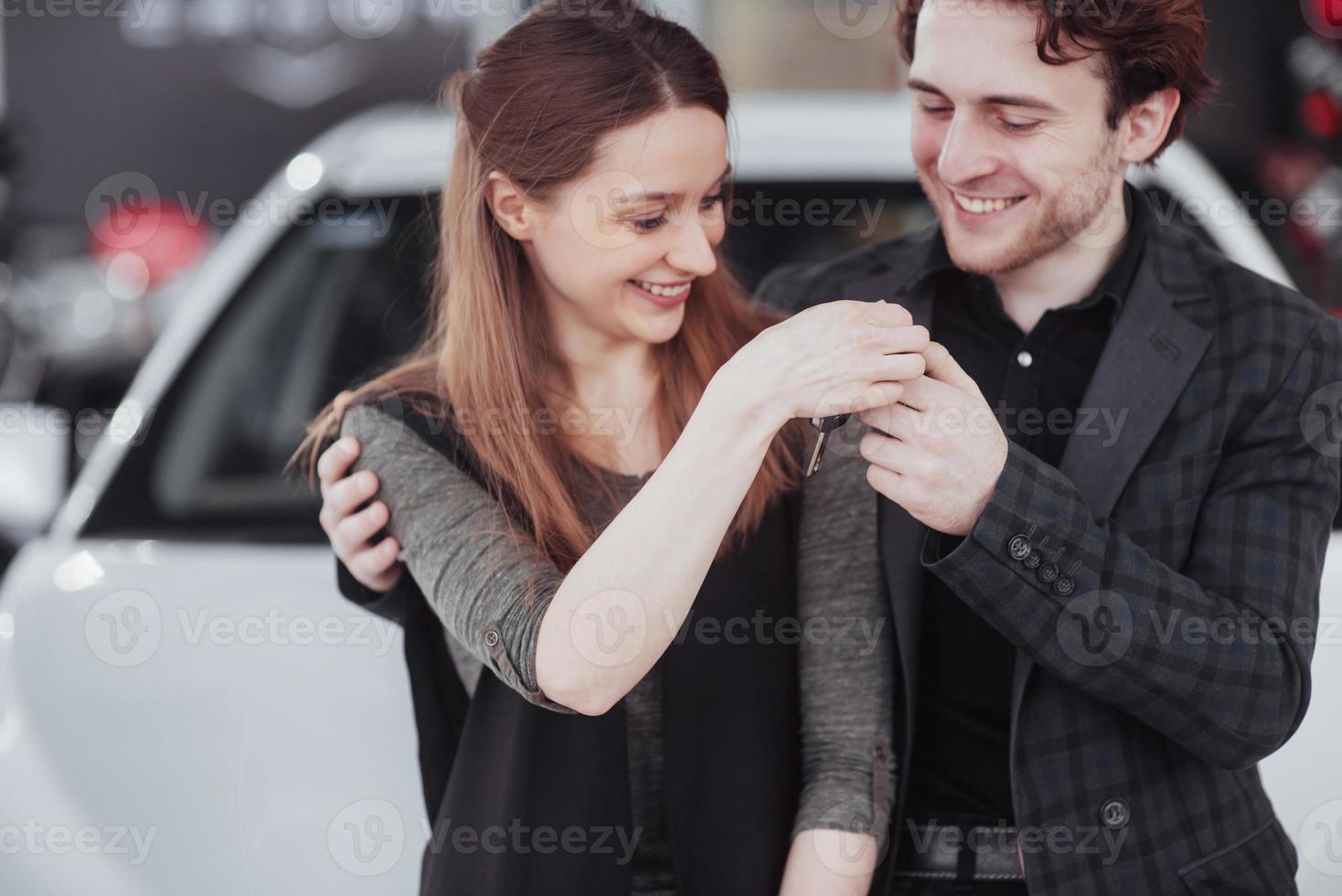 ahora su sueño se hace realidad. vendedor de coches dando la llave del coche nuevo a los jóvenes propietarios atractivos foto