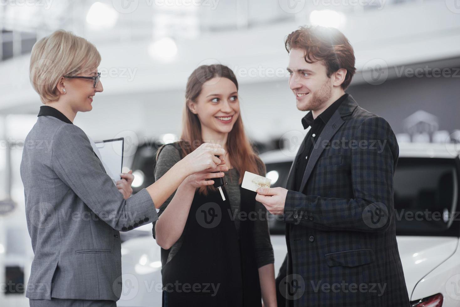 listo para montar. Hermosa pareja amorosa posando juntos cerca de su auto nuevo en el salón de exposición del concesionario de autos sonriendo felizmente mostrando las llaves de su auto transporte alquiler de vehículos comprando bienestar estilo de vida foto