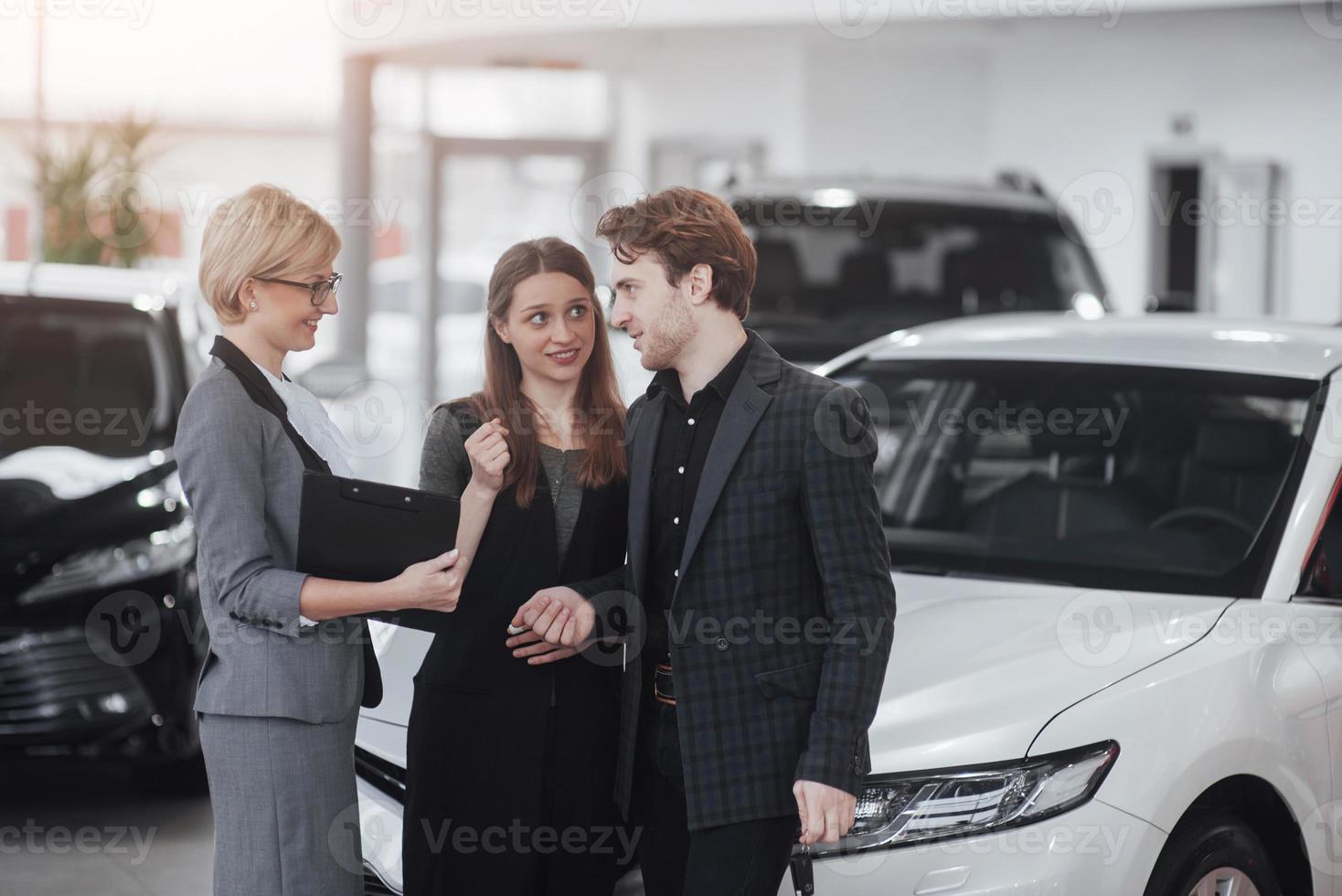 comprando su primer auto juntos. Un alto ángulo de vista del joven vendedor de automóviles de pie en el concesionario y contar las características del automóvil a los clientes. foto