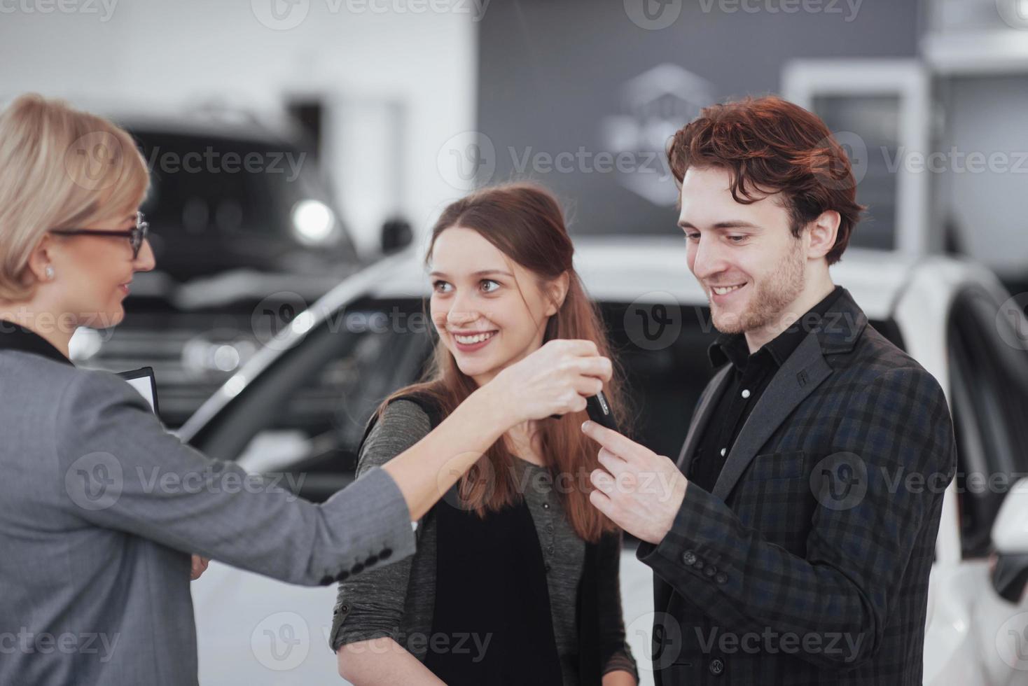 comprando su primer auto juntos. Un alto ángulo de vista del joven vendedor de automóviles de pie en el concesionario y contar las características del automóvil a los clientes. foto