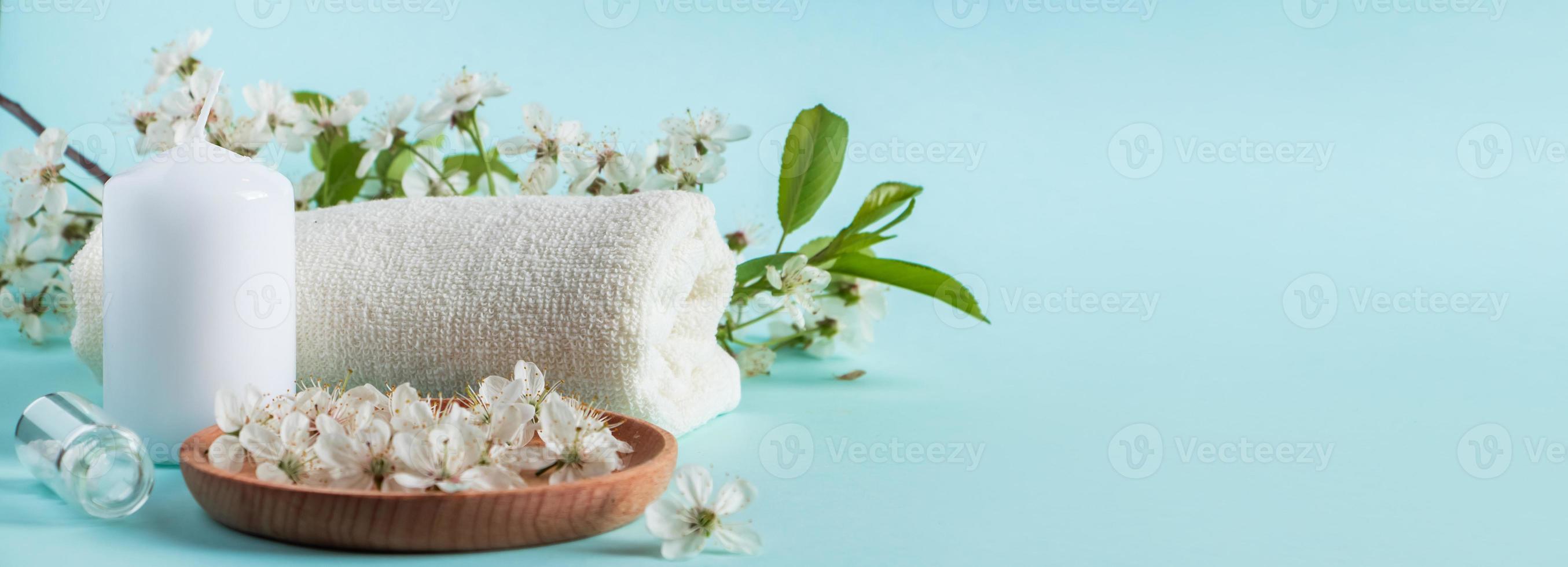 Aromatherapy wellness concept. Spa and relaxation accessories on blue background. Aromatic oil, towel, candle and flowers. Organic skin care product. photo