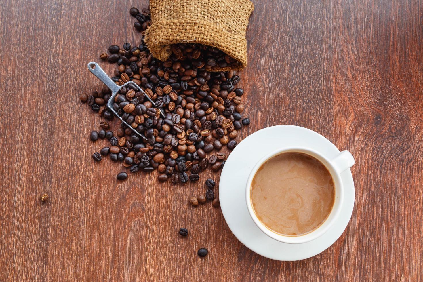 Taza de café y granos de café en un saco sobre fondo marrón, vista superior foto