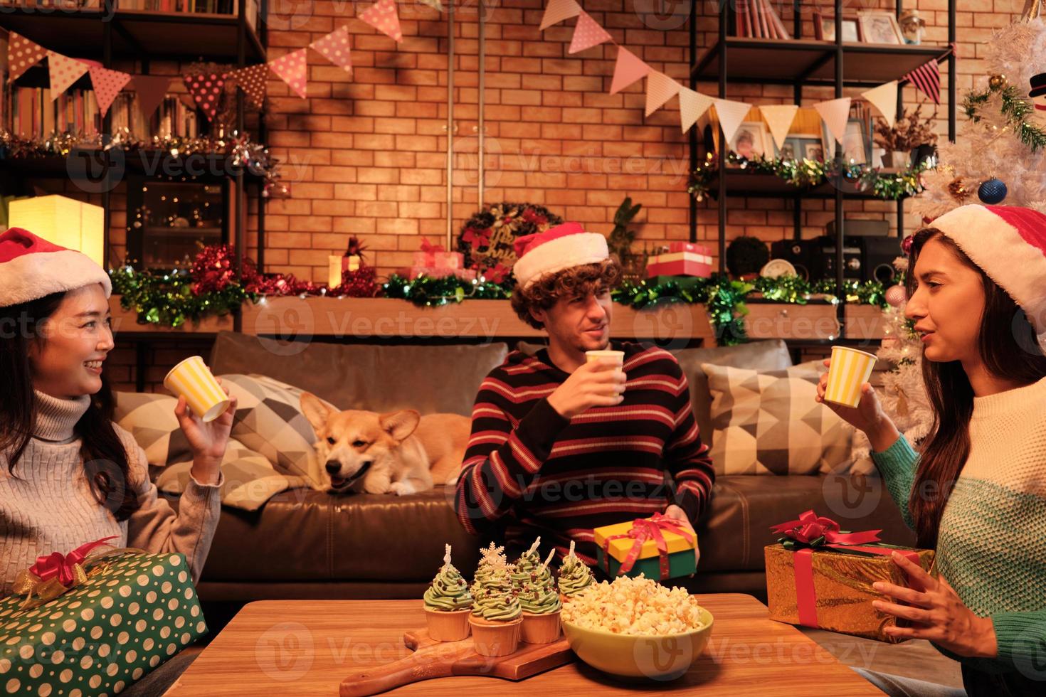 Sorprenda a tres amigos y familiares dándoles regalos juntos e intercambiándolos mientras las felices vacaciones en la sala de estar de su casa están decoradas para la celebración del festival navideño y la fiesta de año nuevo. foto