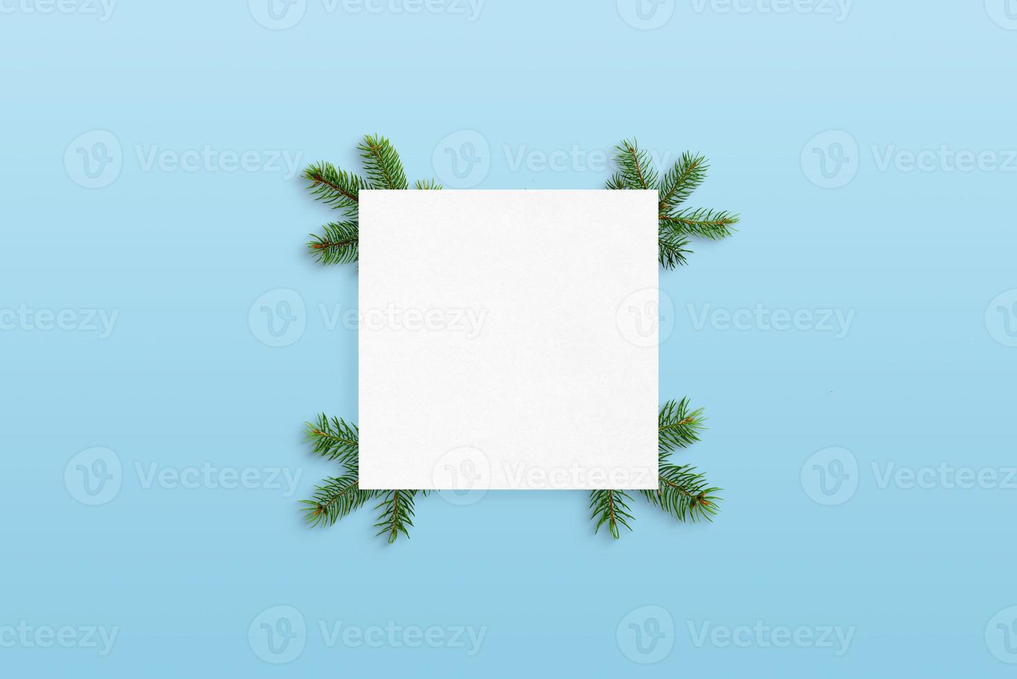 papel en blanco decorado con ramas de árboles de Navidad sobre superficie azul pastel. maqueta de tarjeta de felicitación foto