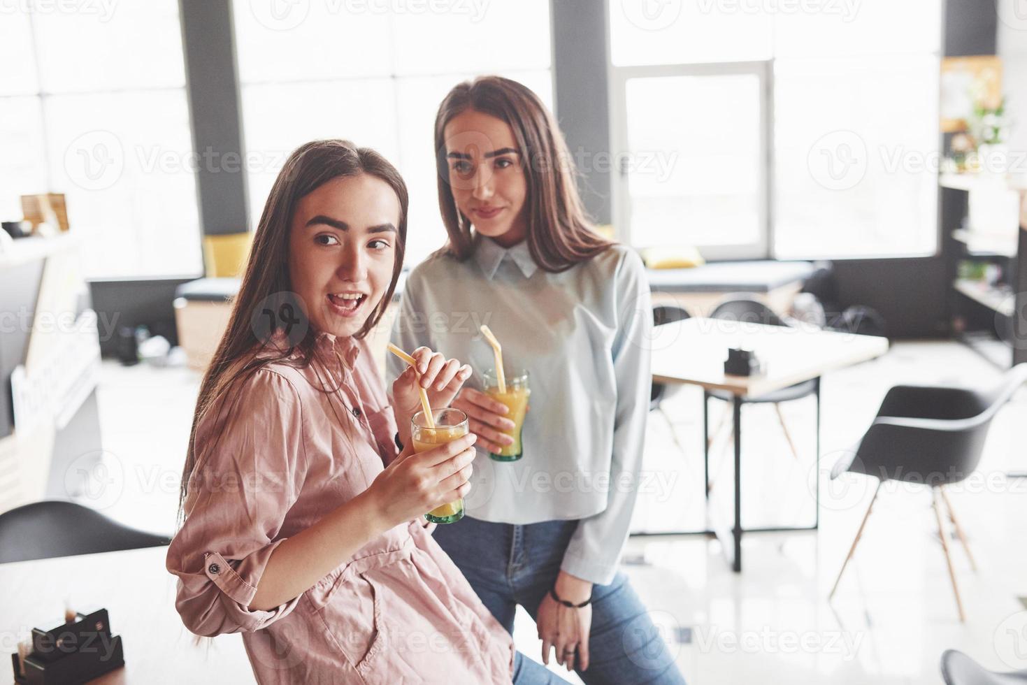 dos hermosas gemelas pasan tiempo bebiendo jugo. hermanas relajándose en un café y divirtiéndose juntas foto